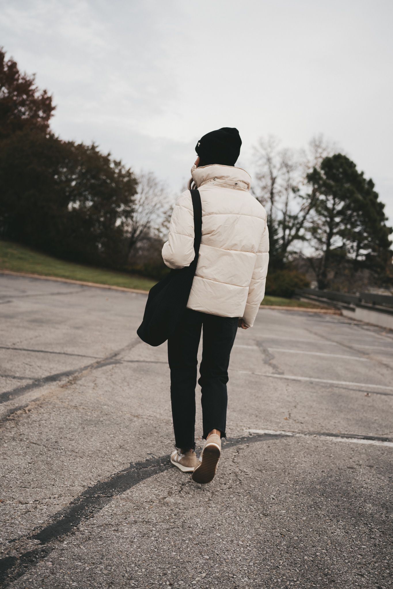 ashley wearing a white puffer coat, black jeans, white and tan sneakers, black beanie, and black tote bag