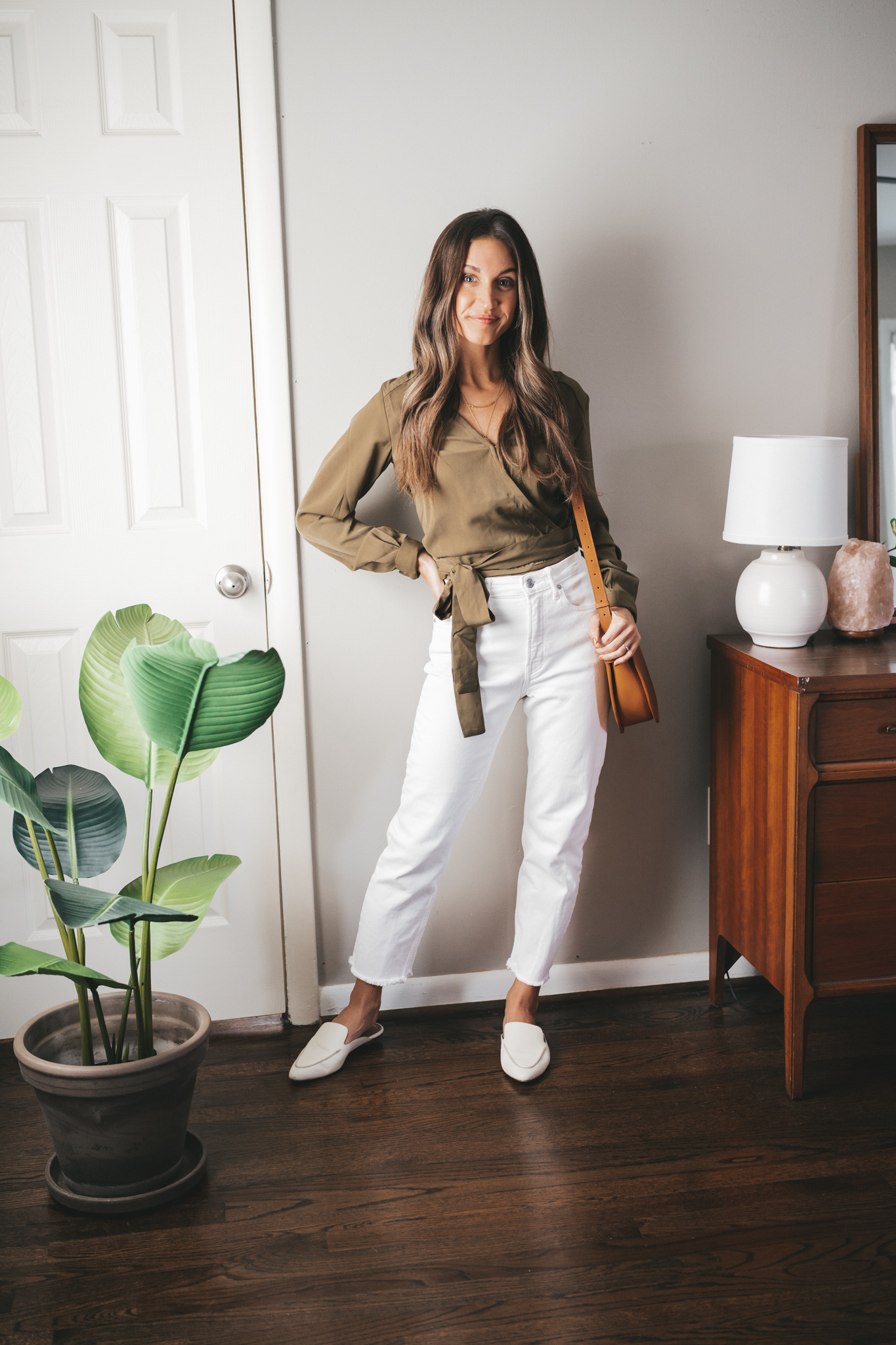 fall outfit idea with a green wrap top, white denim, white mules and a cognac crossbody bag