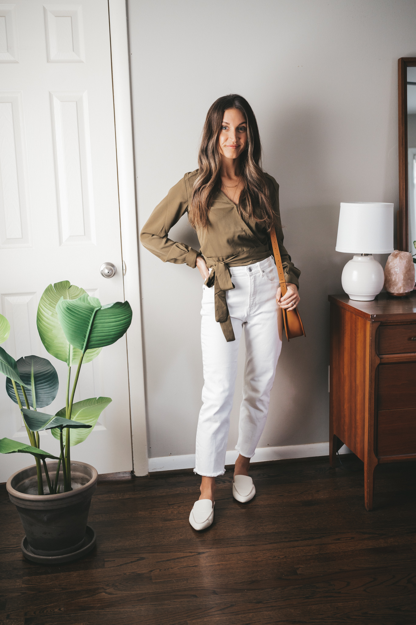 fall outfit idea with a green wrap top, white denim, white mules and a cognac crossbody bag