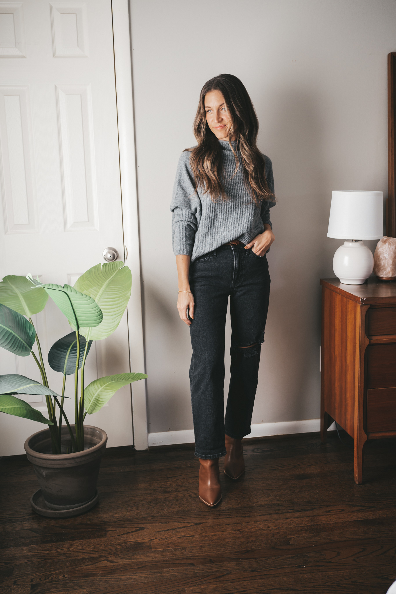 fall outfit idea with an oversized gray sweater, black distressed denim, cognac ankle boots, and a cognac belt