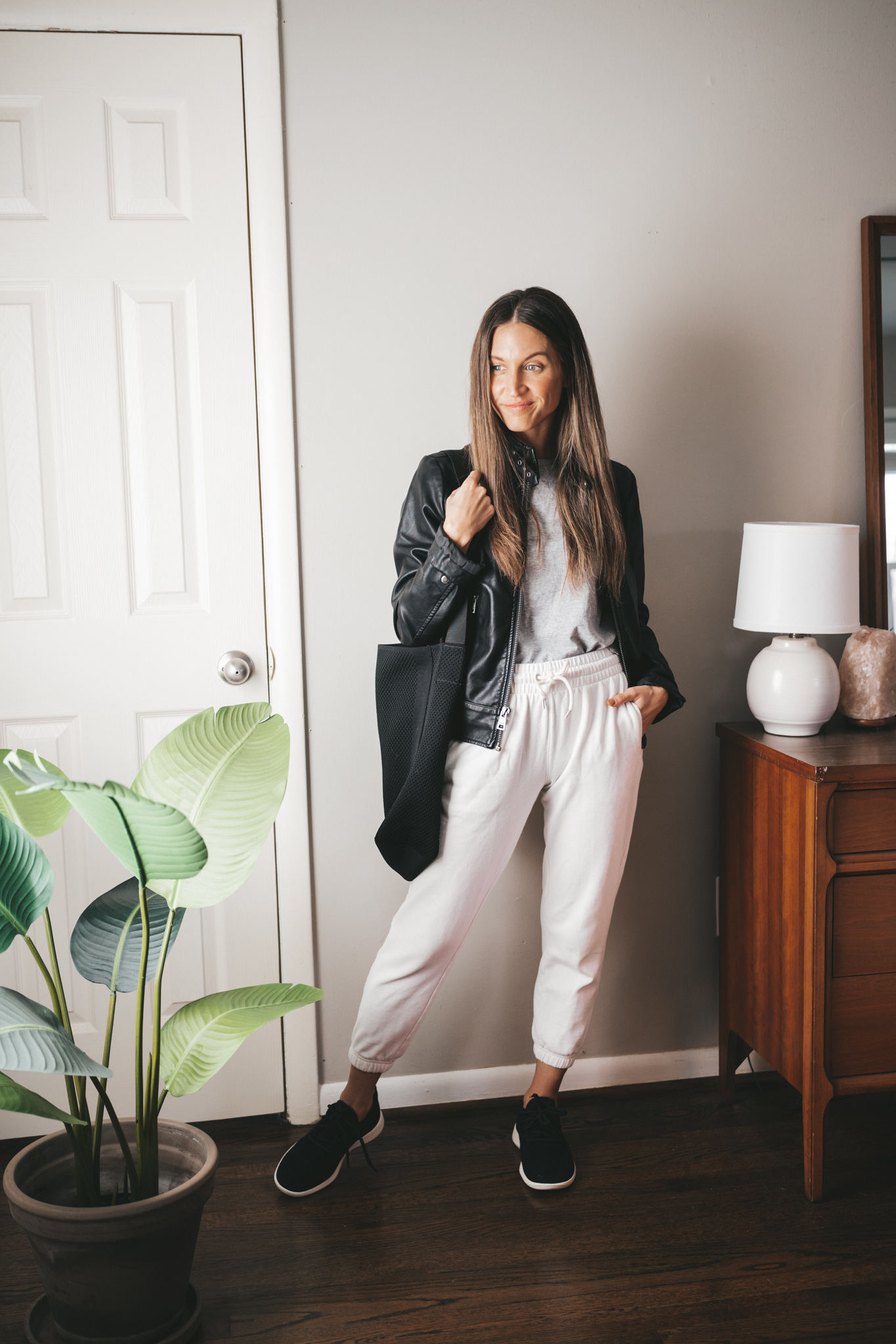 fall outfit idea with white joggers, gray tee, black faux leather moto jacket, black wool runners, and a black tote bag