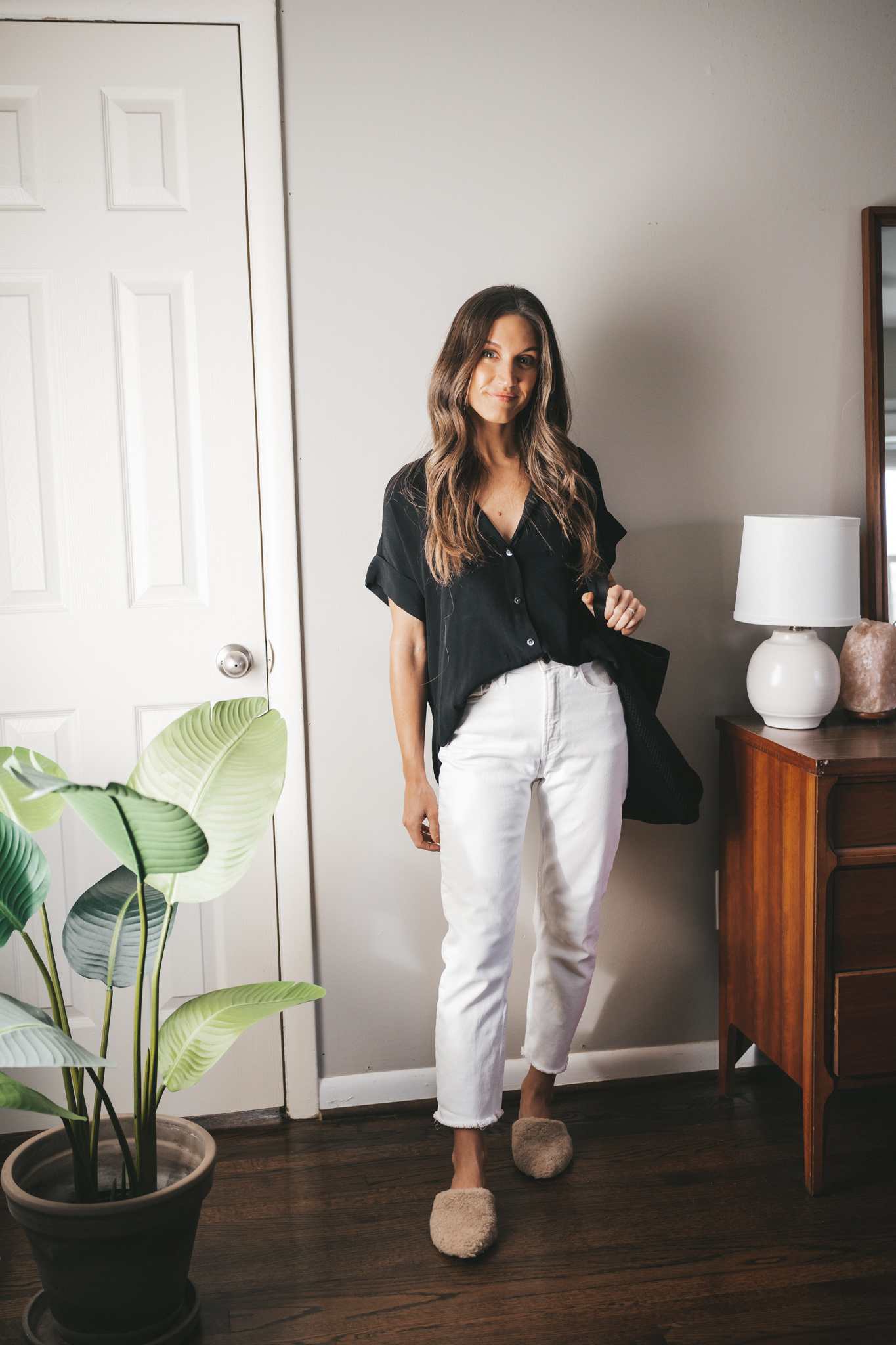 fall outfit idea with an oversized drapey black button down, white denim, tan shearling mules, and a black tote bag