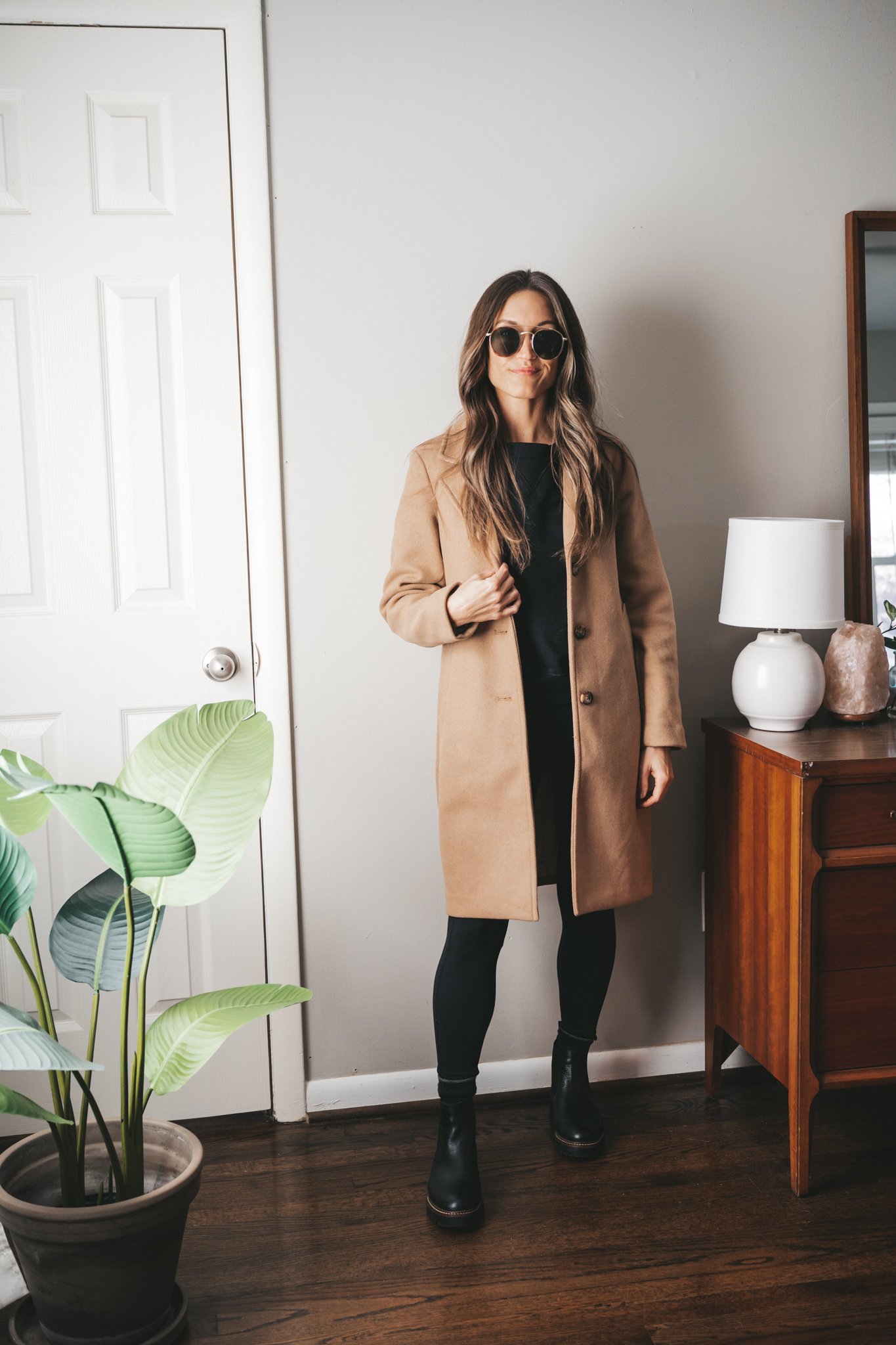 leggings outfit idea with a black sweatshirt, camel coat, black leggings, and black lug sole boots