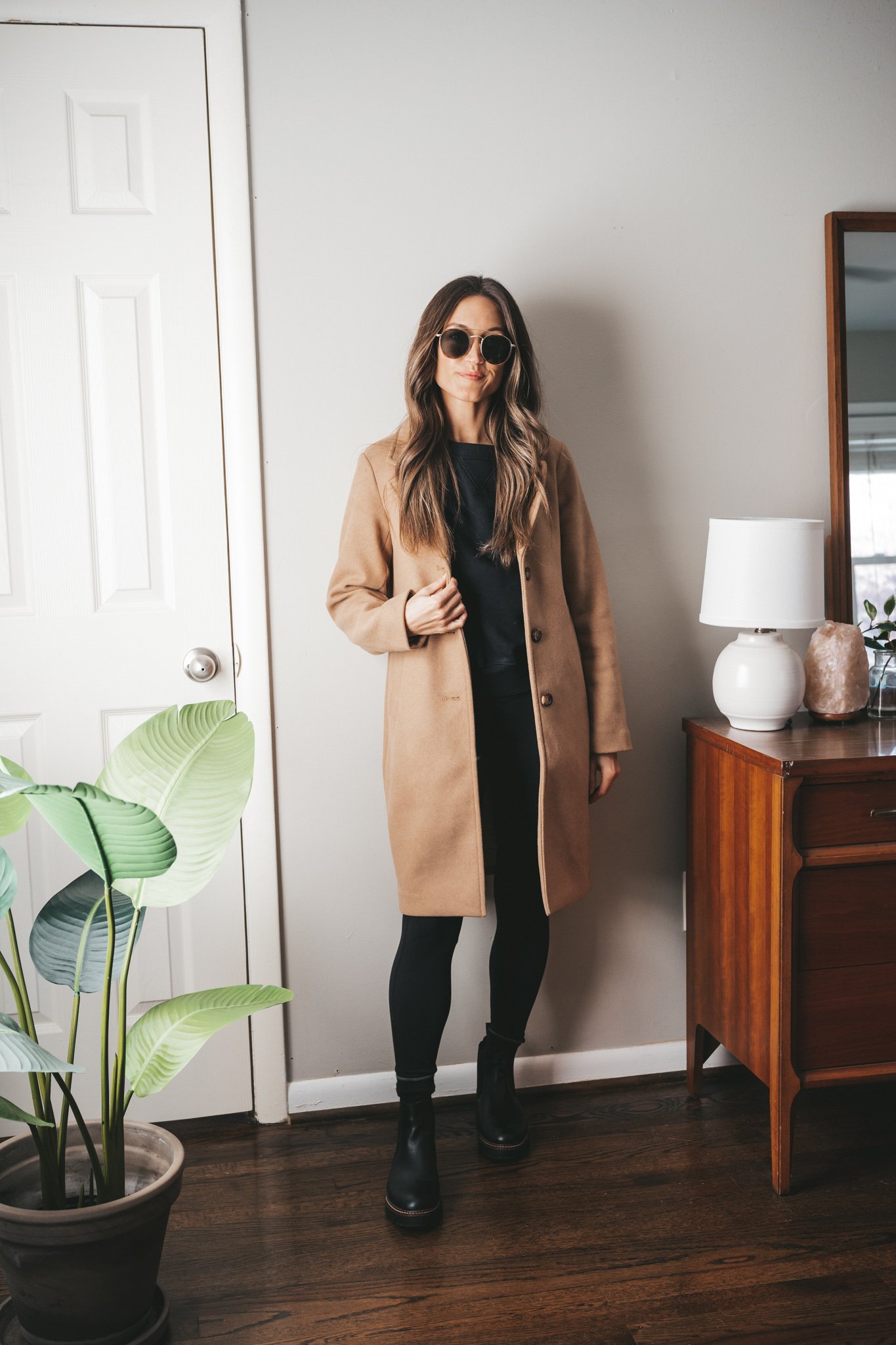 leggings outfit idea with a black sweatshirt, camel coat, black leggings, and black lug sole boots