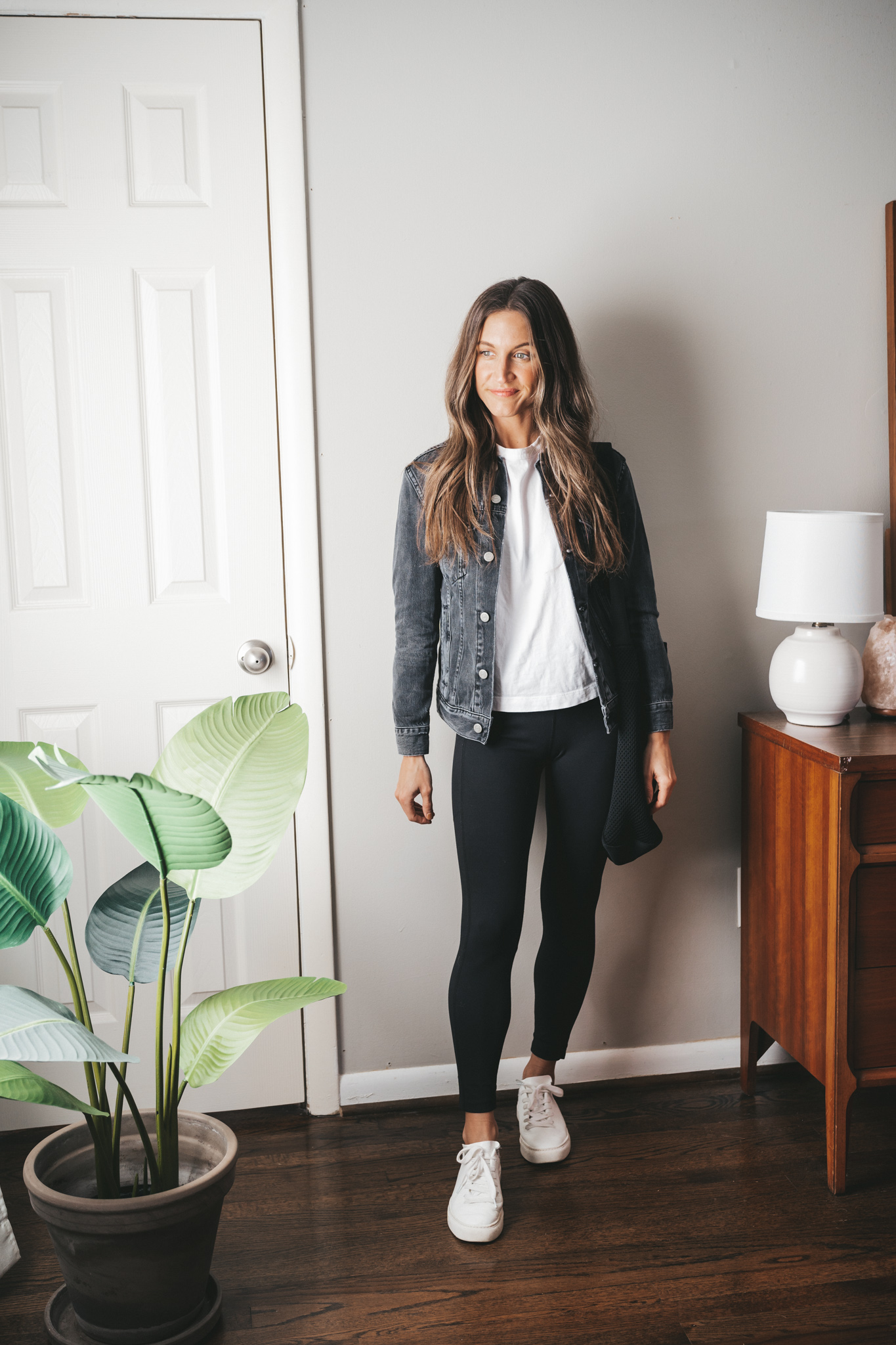 leggings outfit idea with a white tee, washed black denim jacket, black leggings, white sneakers and a black tote bag