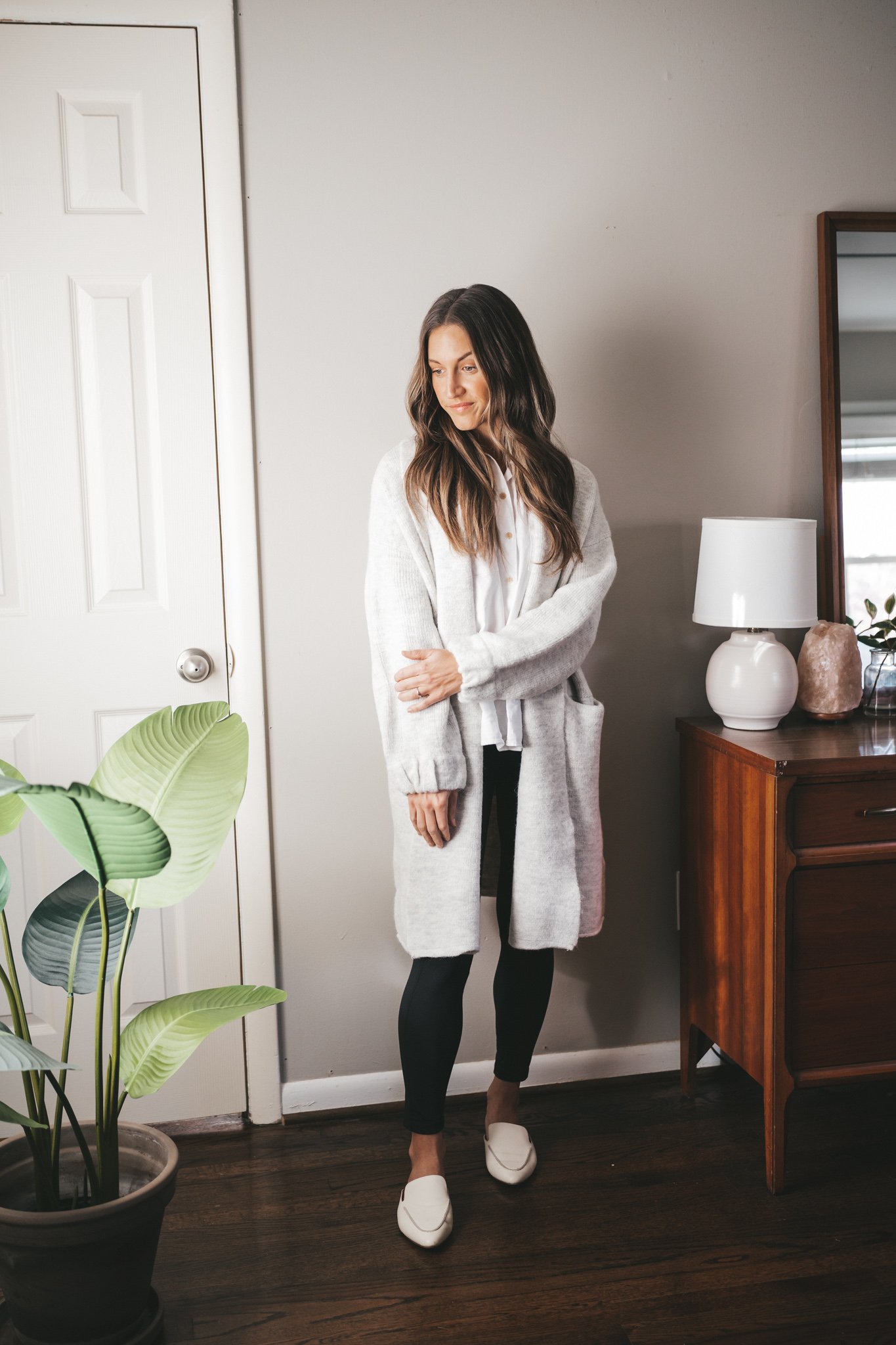 leggings outfit idea with an oversized white button down, gray sweater coat, black leggings, and white mules