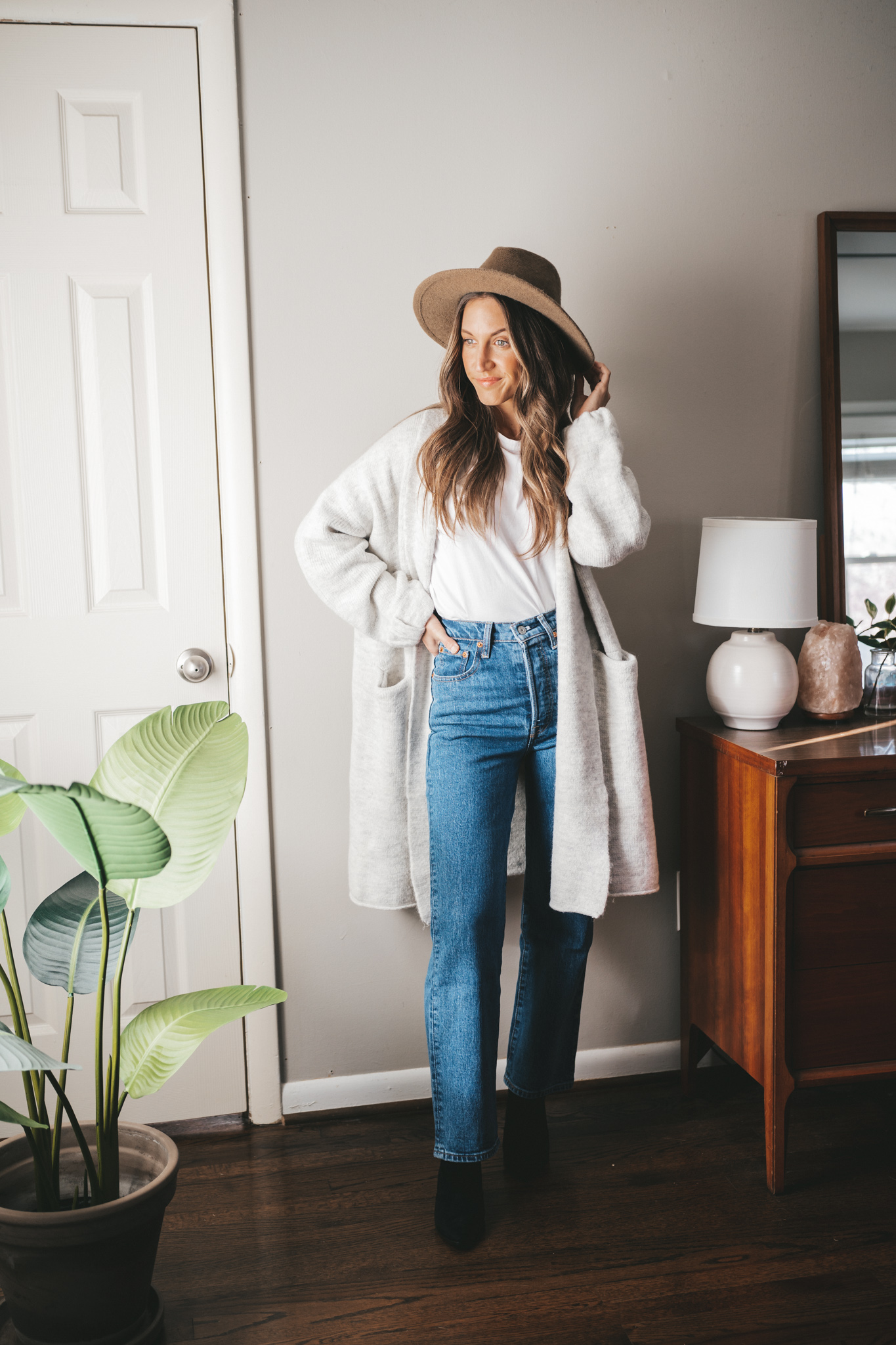 fall outfit idea with a gray sweater coat, white tee, mid-wash straight denim, black heeled booties, and a taupe felt fedora hat