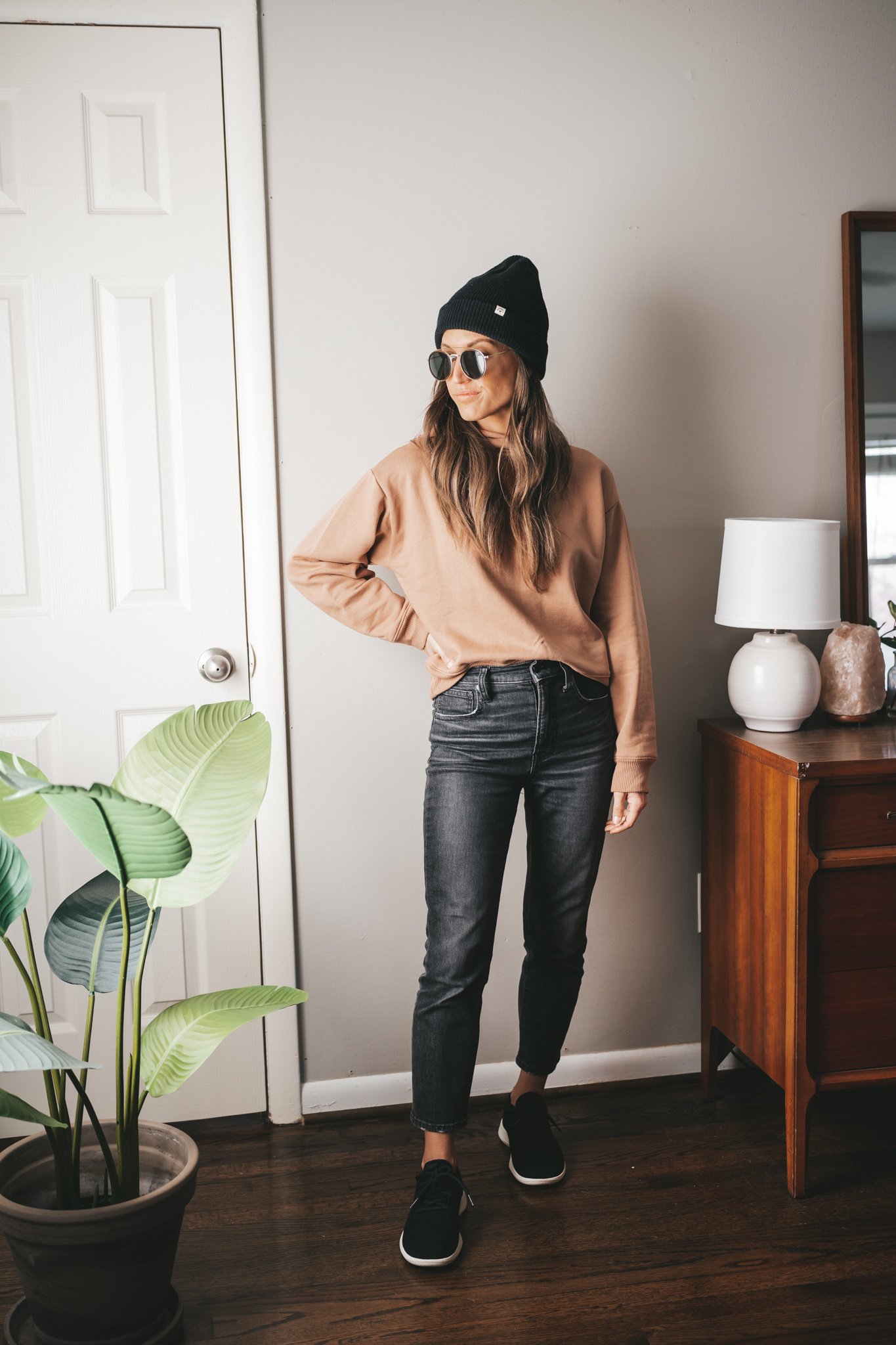 fall outfit idea with a light brown hoodie sweatshirt, washed black denim, black wool runners, black beanie and round gold frame sunglasses