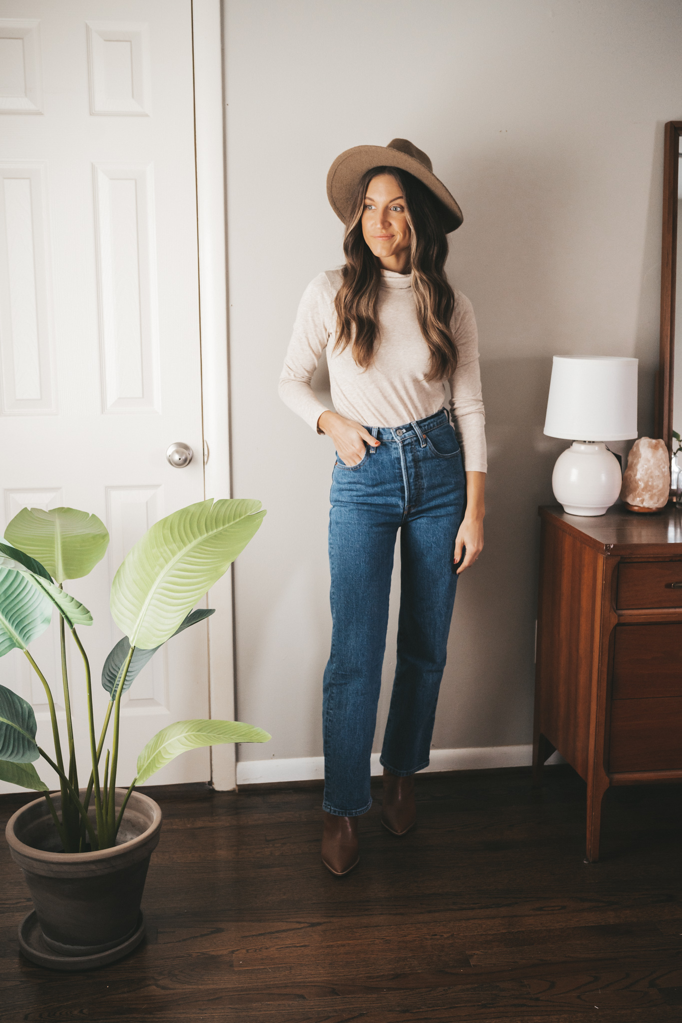 ashley showing one way to style a turtleneck with a mid-wash straight denim, heeled ankle boots, and a felt fedora hat