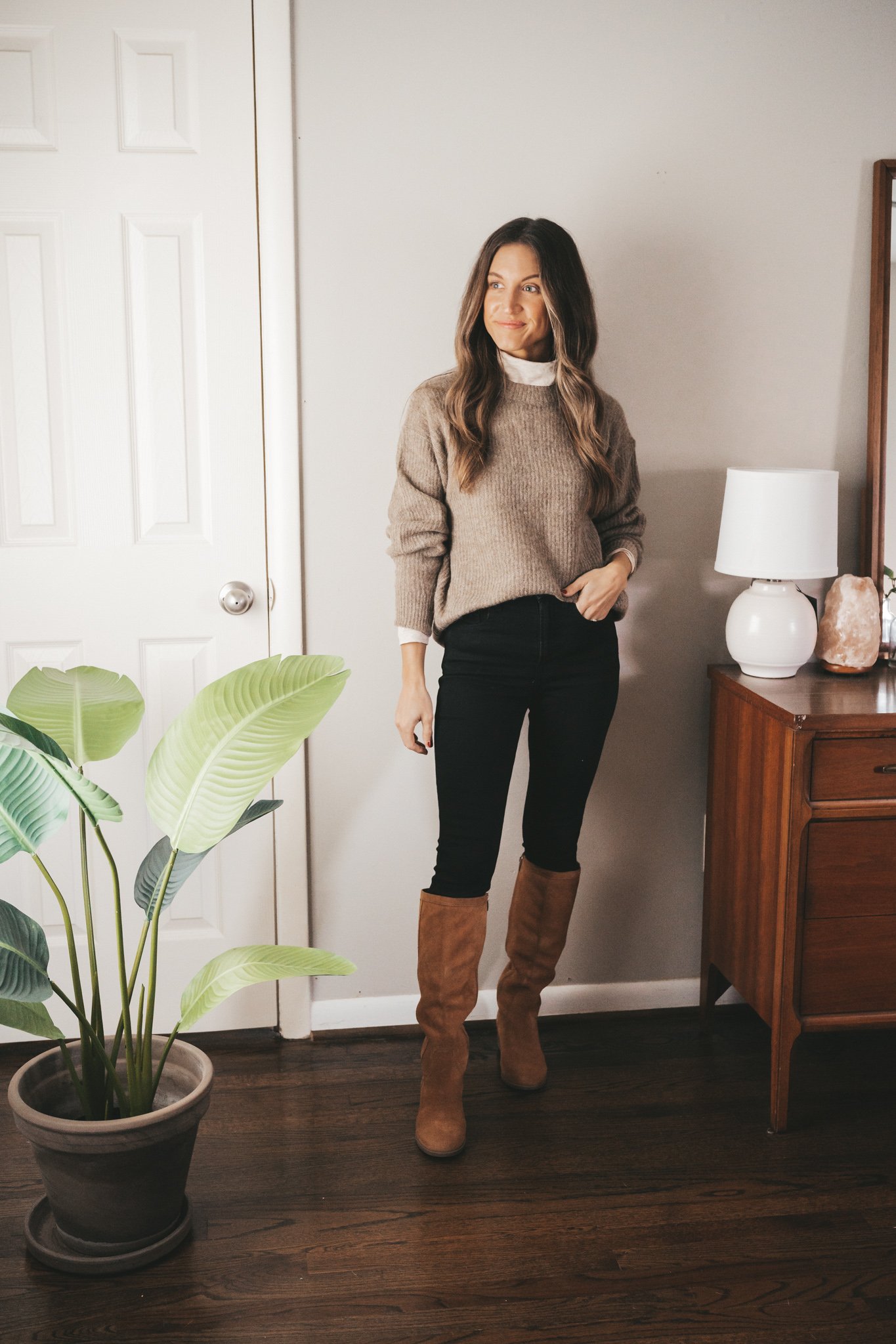 ashley showing one way to style a turtleneck with an oversized sweater, skinny black jeans, and cognac knee high boots