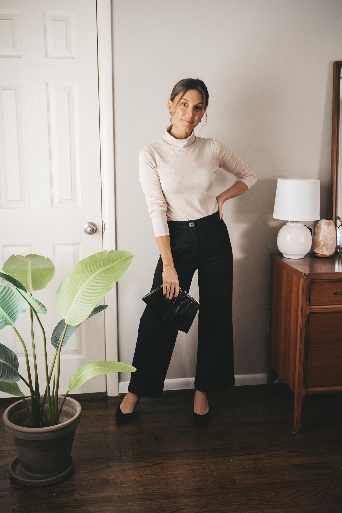 ashley showing one way to style a turtleneck with black wide leg pants, black block heel pumps, and a vintage clutch bag