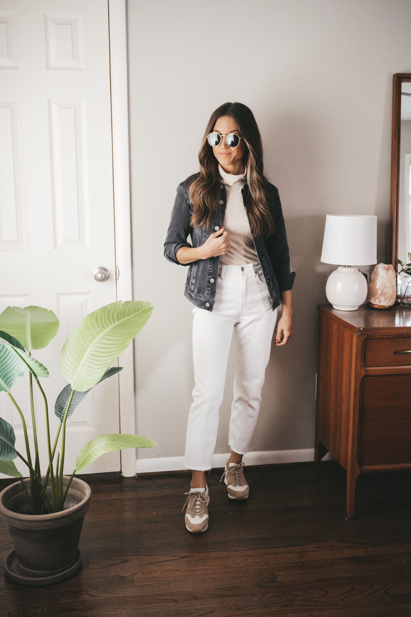 ashley showing one way to style a turtleneck with a washed black denim jacket, white denim, sneakers, and gold round frame sunglasses