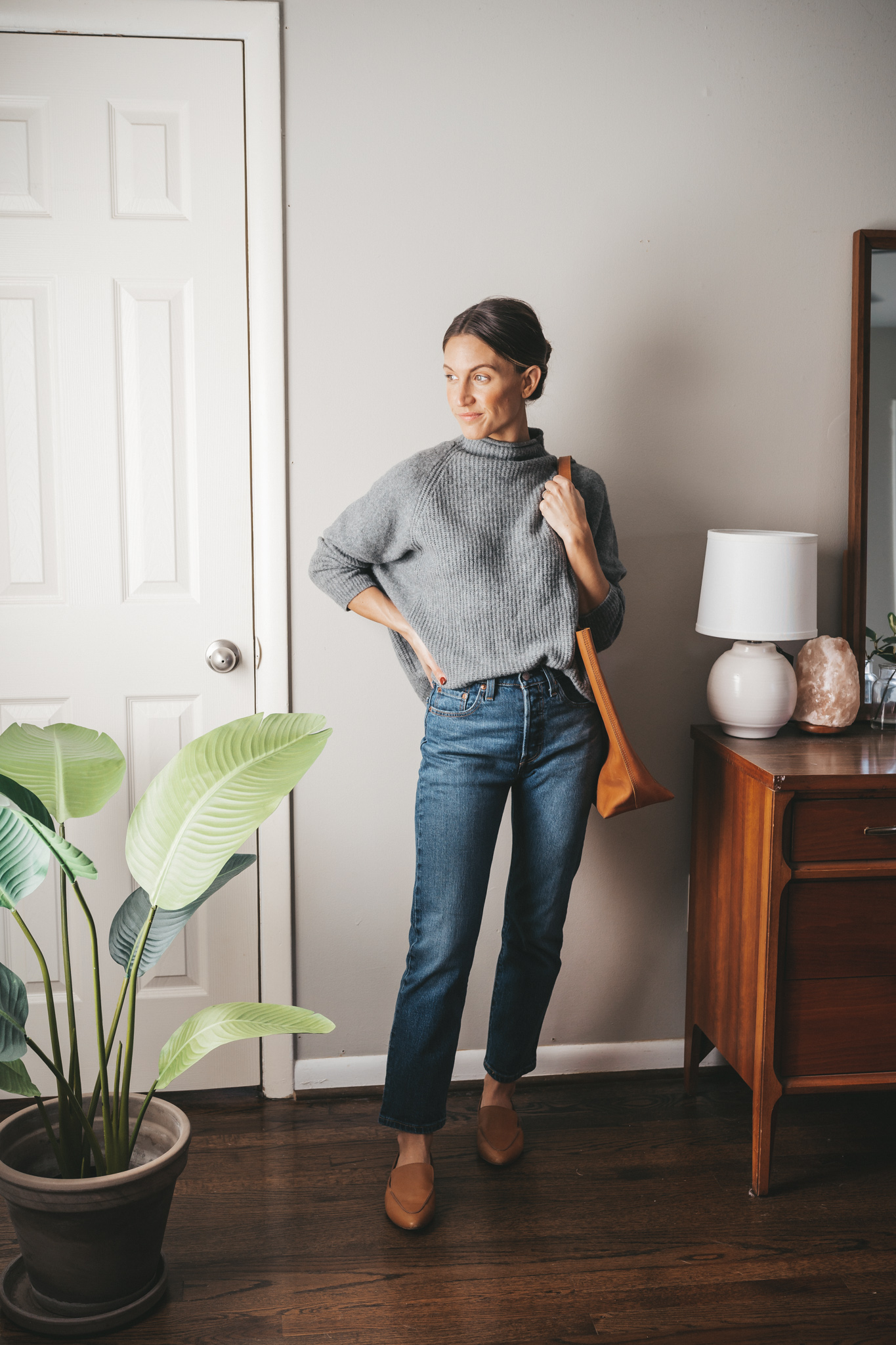 winter outfit idea with a gray mockneck sweater, mid-wash straight denim, cognac loafers and a cognac leather tote bag