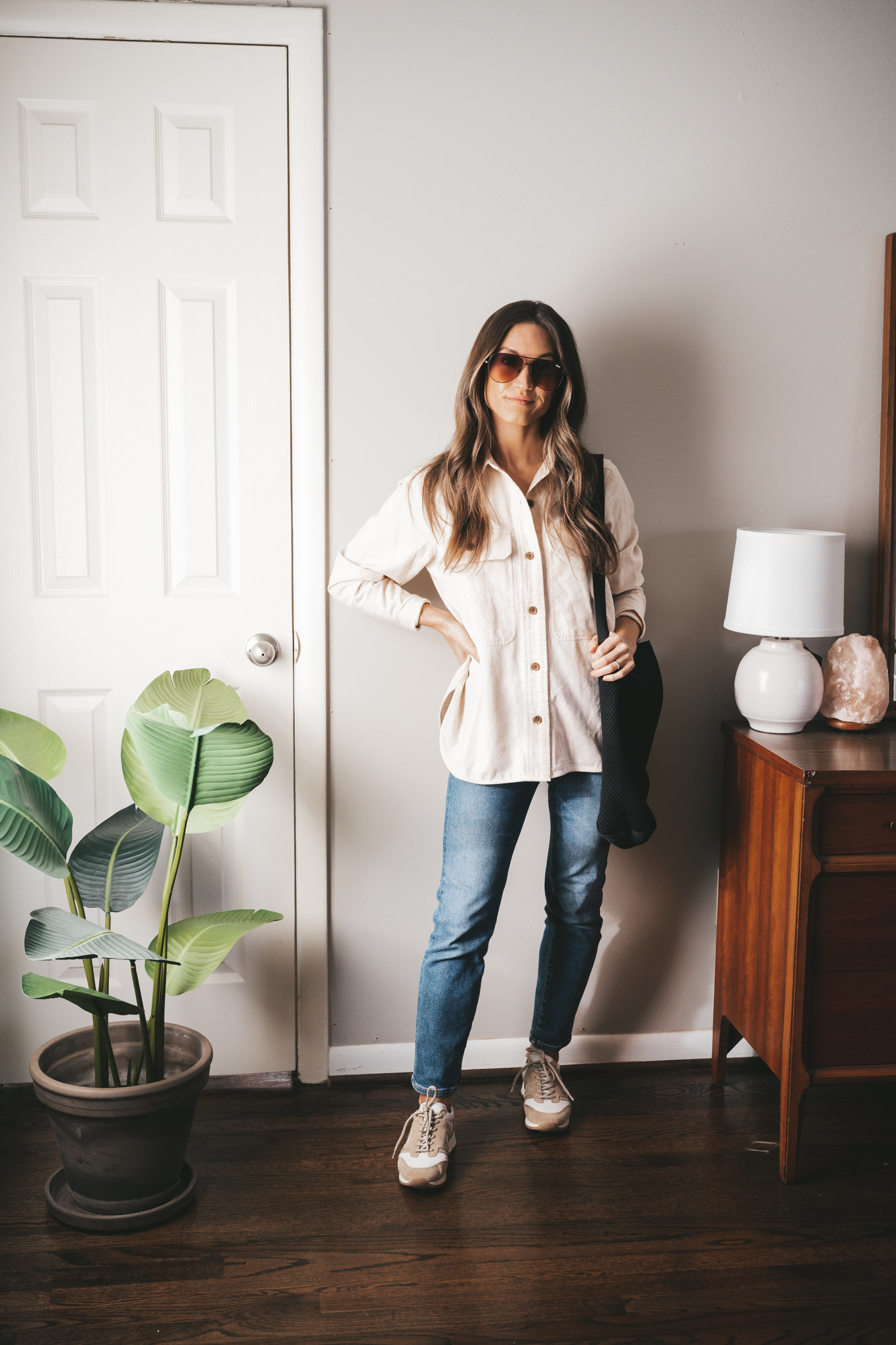 winter outfit idea with a cream colored flannel, mid-wash mom jeans, and white and tan leather sneakers with a black tote bag, and black oversized aviator sunglasses
