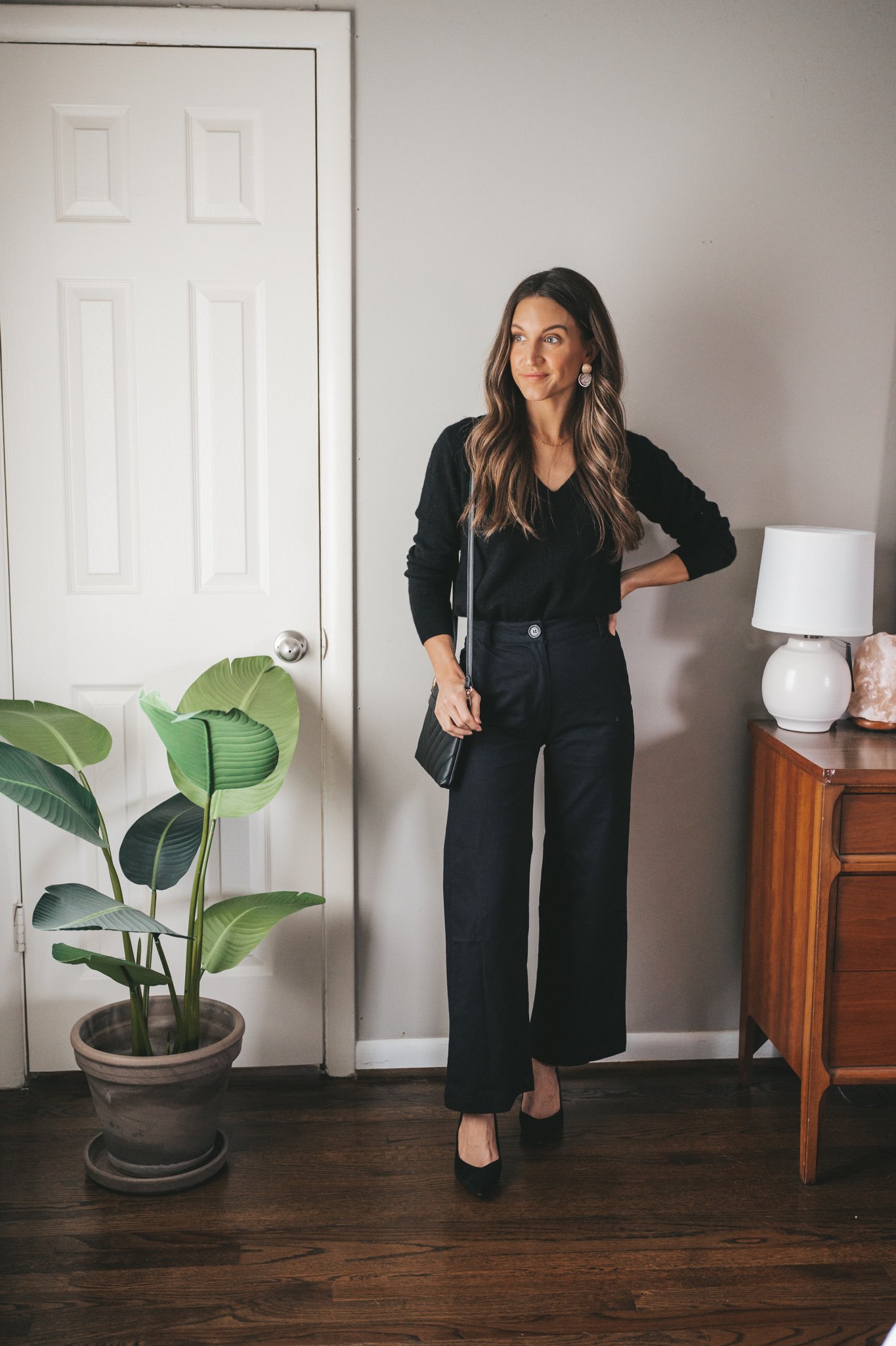 ashley wearing a Christmas Eve outfit idea with a black v-neck sweater, wide leg pants, black block heels, and gold earrings