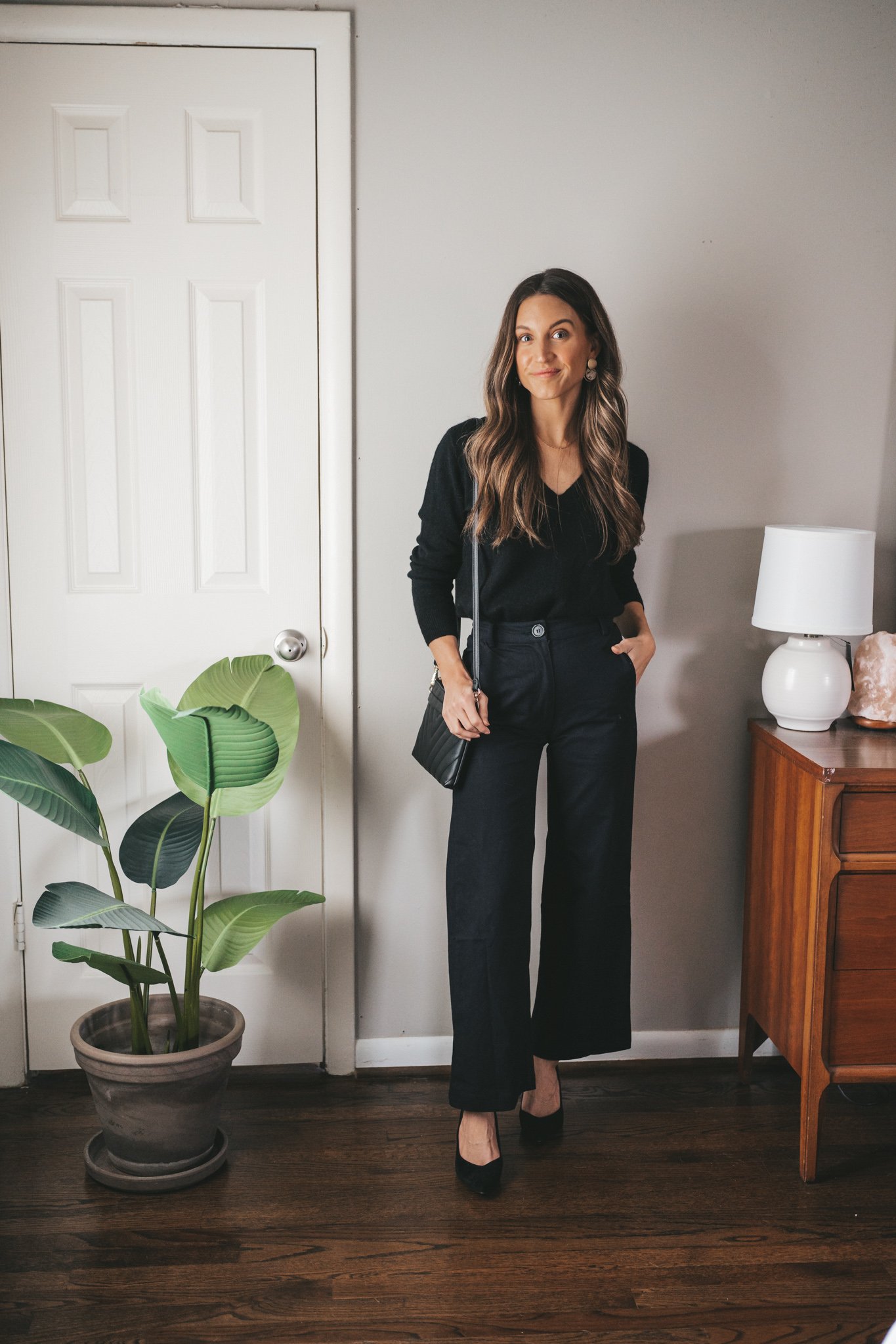 ashley wearing a Christmas Eve outfit idea with a black v-neck sweater, wide leg pants, black block heels, and gold earrings