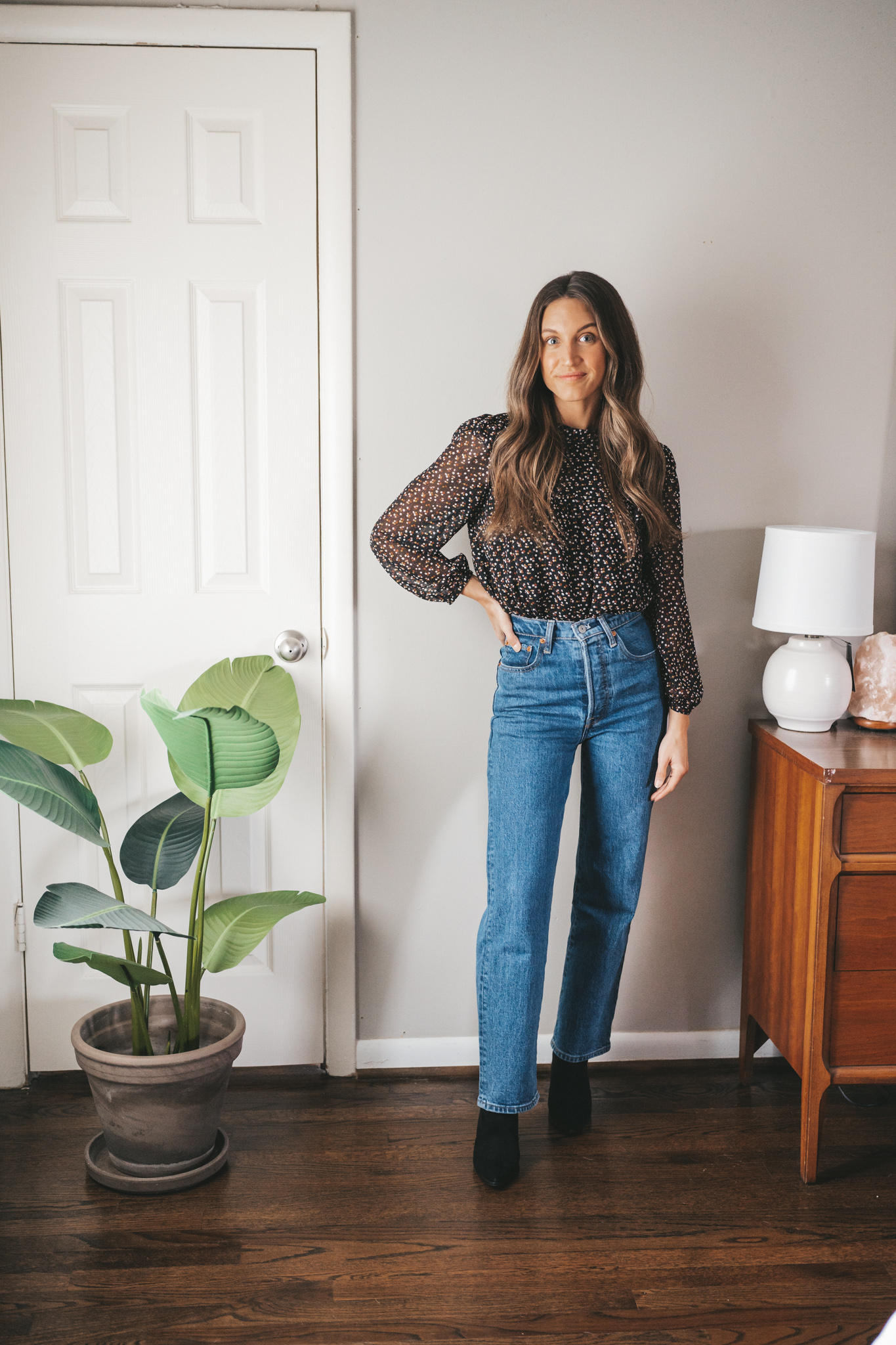 ashley wearing a Christmas Day dinner outfit idea with a black floral blouse, dark wash straight denim, and black suede heeled ankle boots