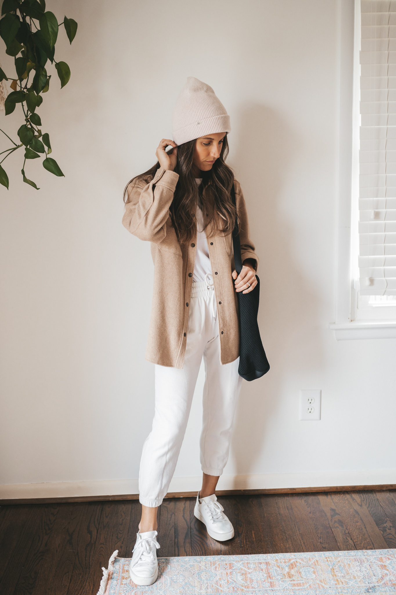 ashley wearing a tan shacket, white tee, white joggers, white sneakers, and a cream colored beanie with a black tote bag