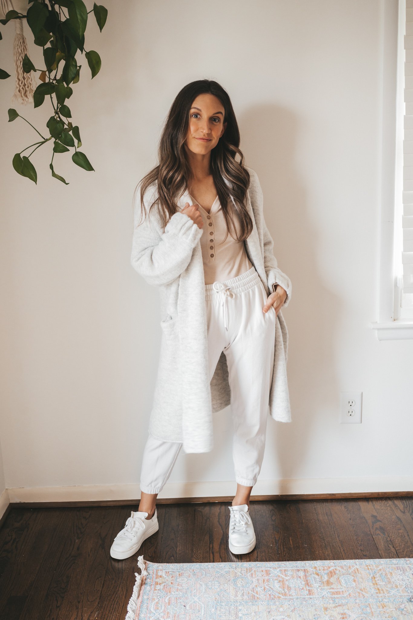 ashley wearing an ivory henley bodysuit, white joggers, and a light gray sweater coat and white sneakers