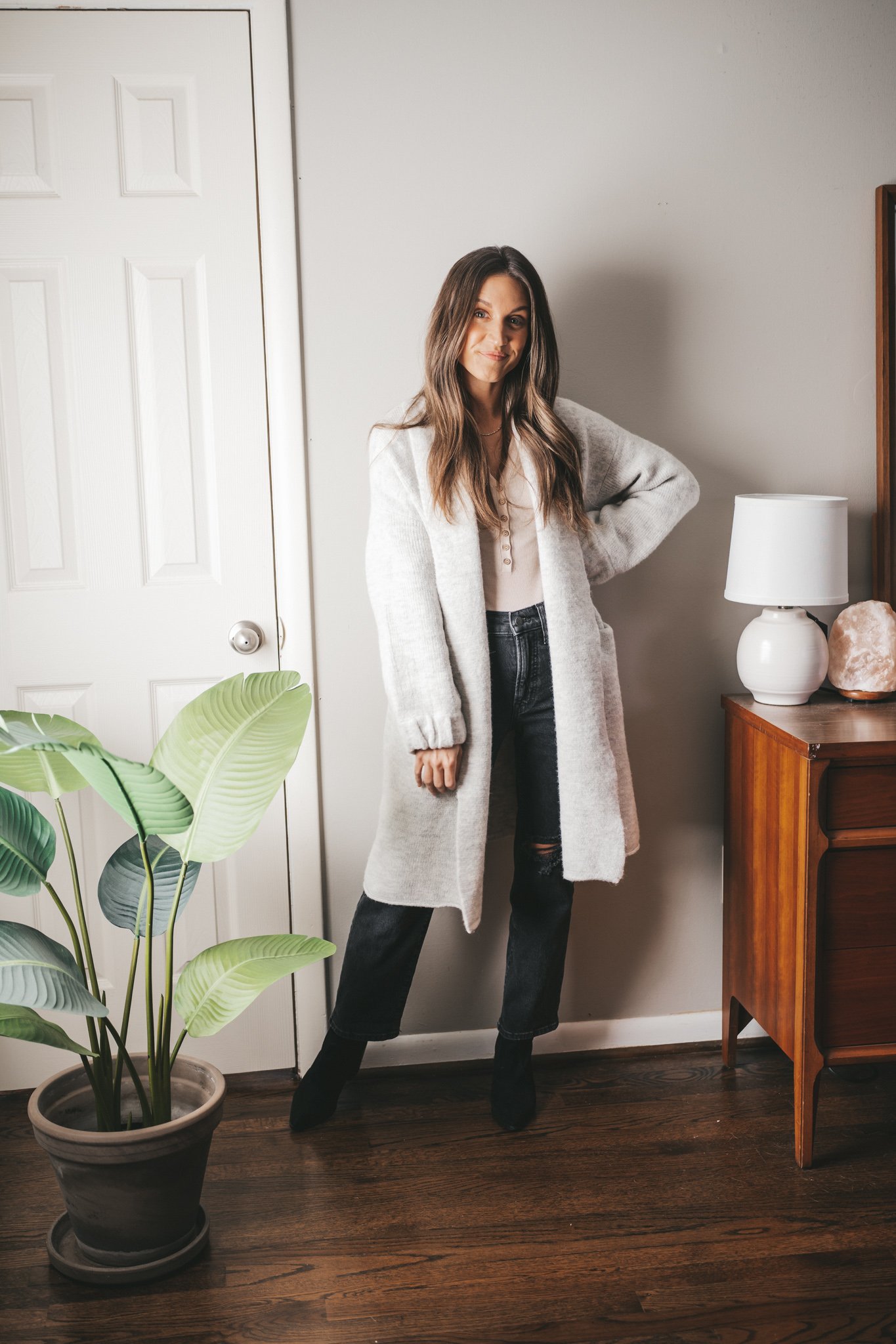 winter outfit idea with a ivory henley bodysuit, light gray sweater coat, washed black distressed denim, and black heeled ankle boots