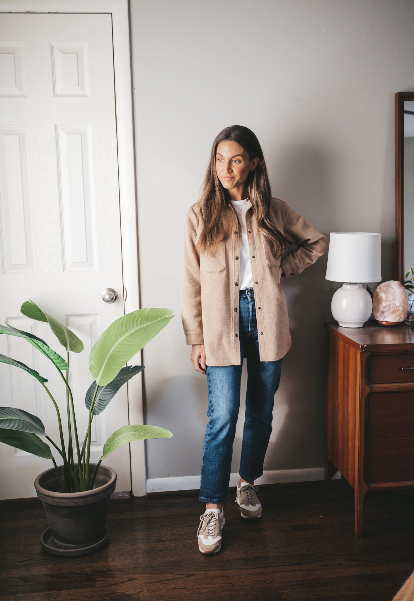 winter outfit idea with a white tee, tan shacket, mid-wash mom jeans, and white and tan leather sneakers