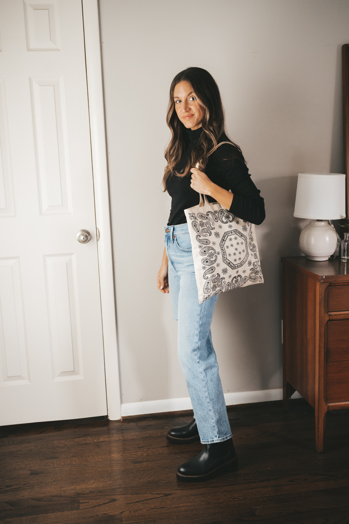 winter essential chelsea boot worn with light wash straight denim, a black turtleneck, and a paisley printed canvas bag