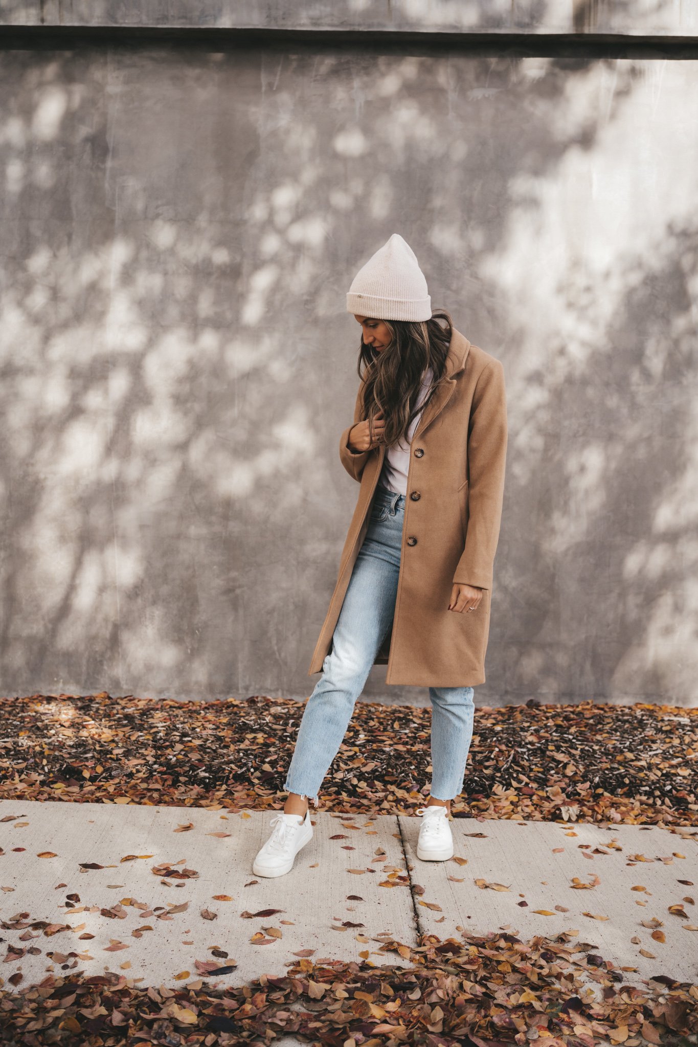 how to style a camel coat with a white tee, light wash denim, white sneakers, and a cream colored beanie