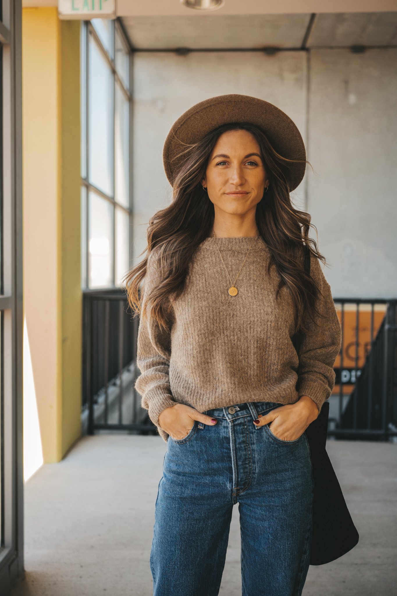ashley wearing a crewneck sweater with denim, a gold coil necklace, and a taupe felt fedora
