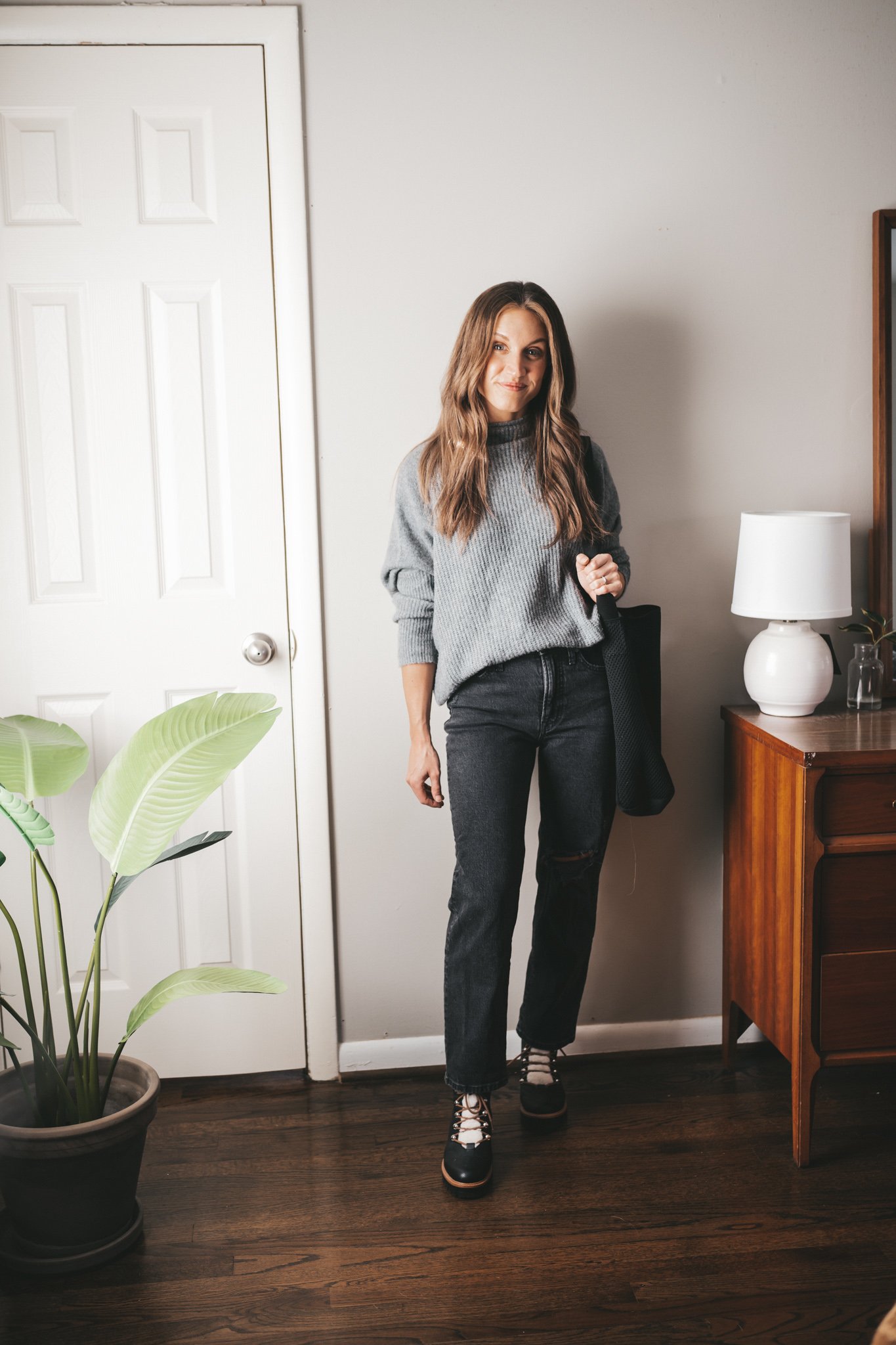 winter capsule wardrobe outfit idea with a gray sweater, black distressed denim, faux shearling winter boots, and black tote bag