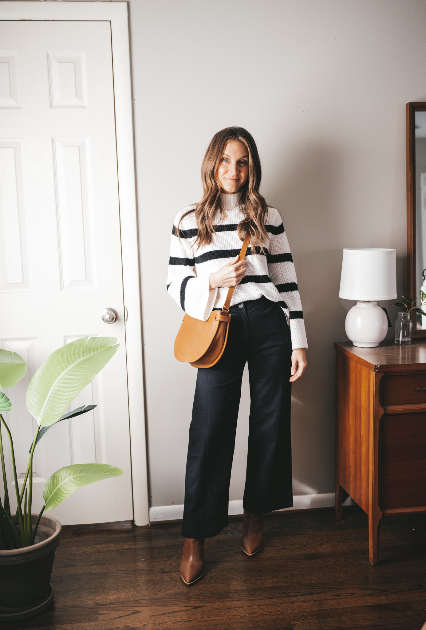 winter capsule wardrobe outfit idea with a black and white striped sweater, wide leg black pants, brown heeled ankle boots, and a cognac crossbody bag