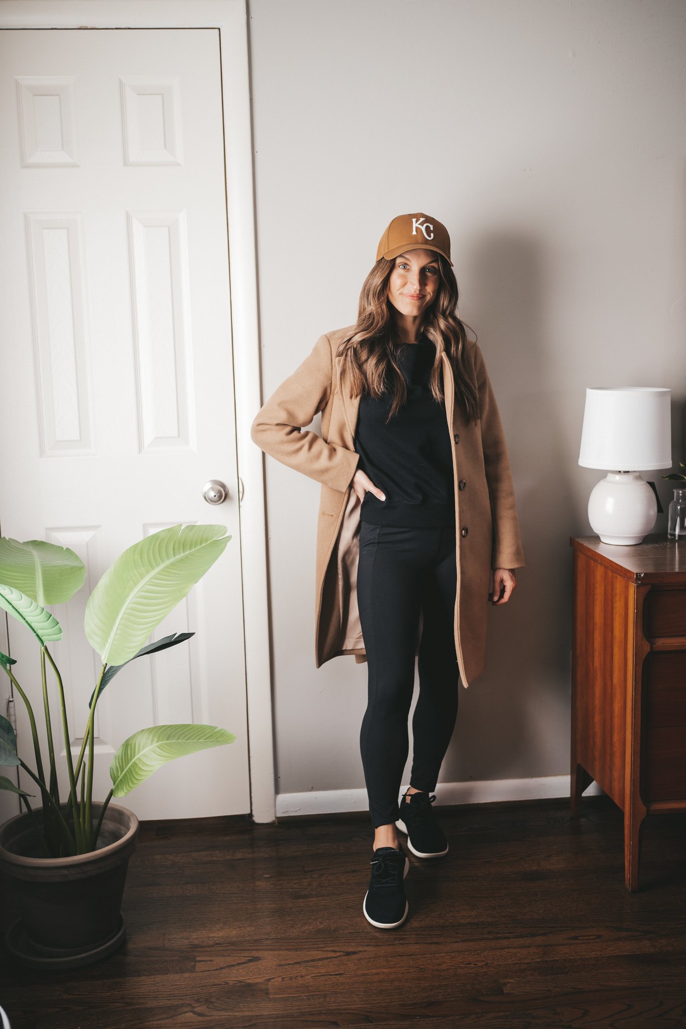a casual winter outfit idea with a black sweatshirt, black leggings, black wool sneakers, and a Carhartt brown KC baseball hat