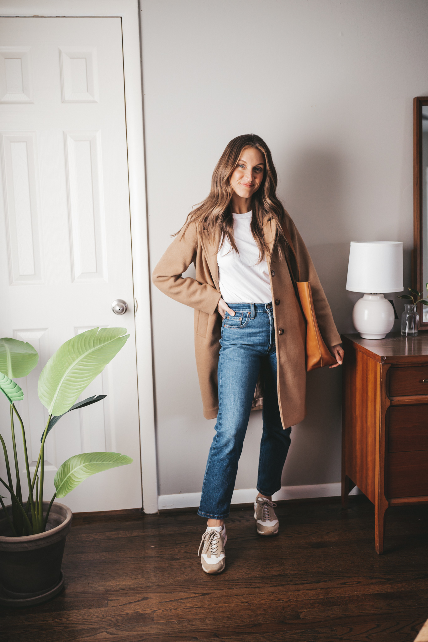 a casual outfit with a camel coat, denim, white and tan leather sneakers, and a cognac leather tote bag