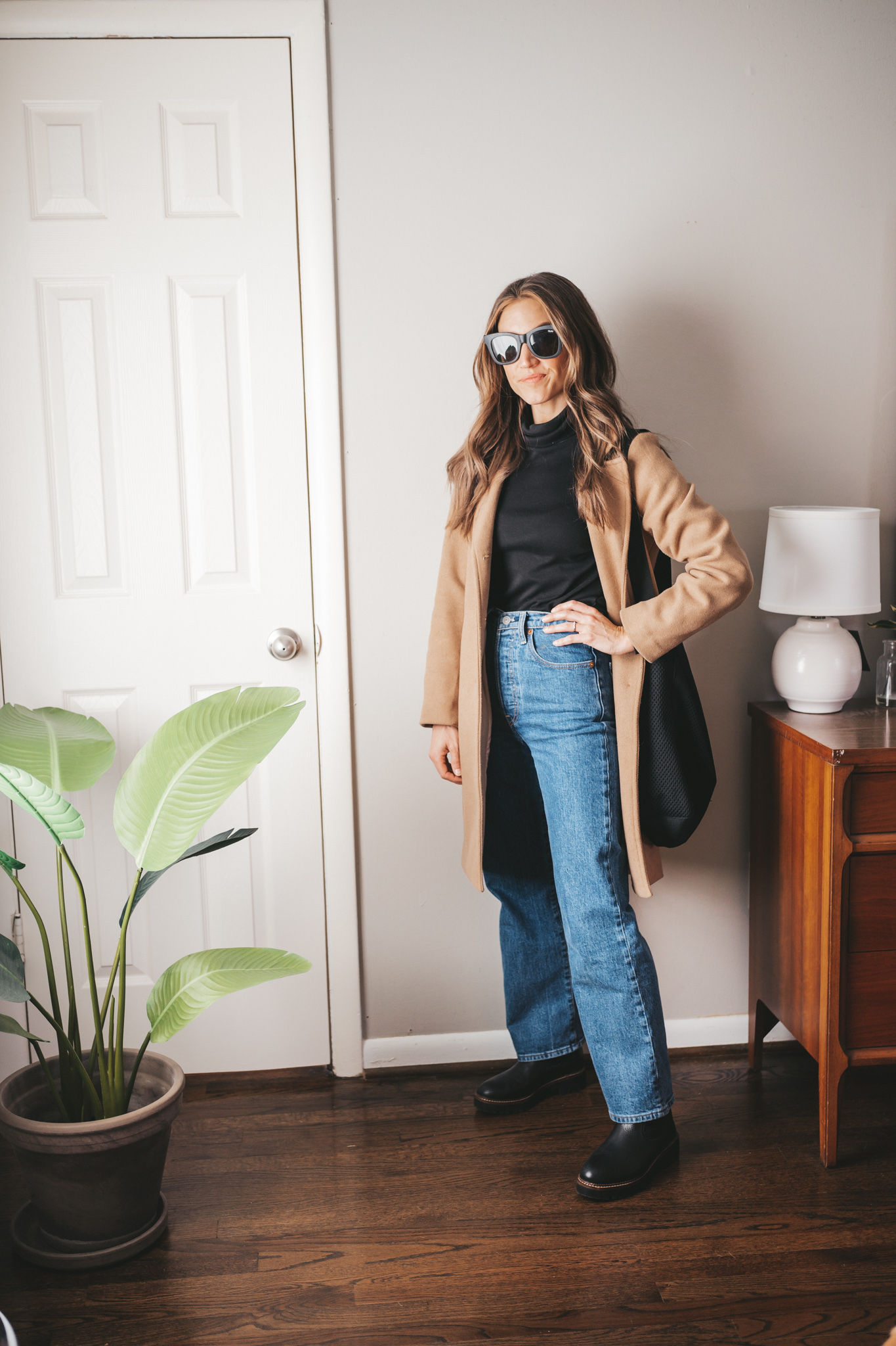 how to style a camel coat with a black turtleneck, denim, black lug sole boots, and black square frame sunglasses