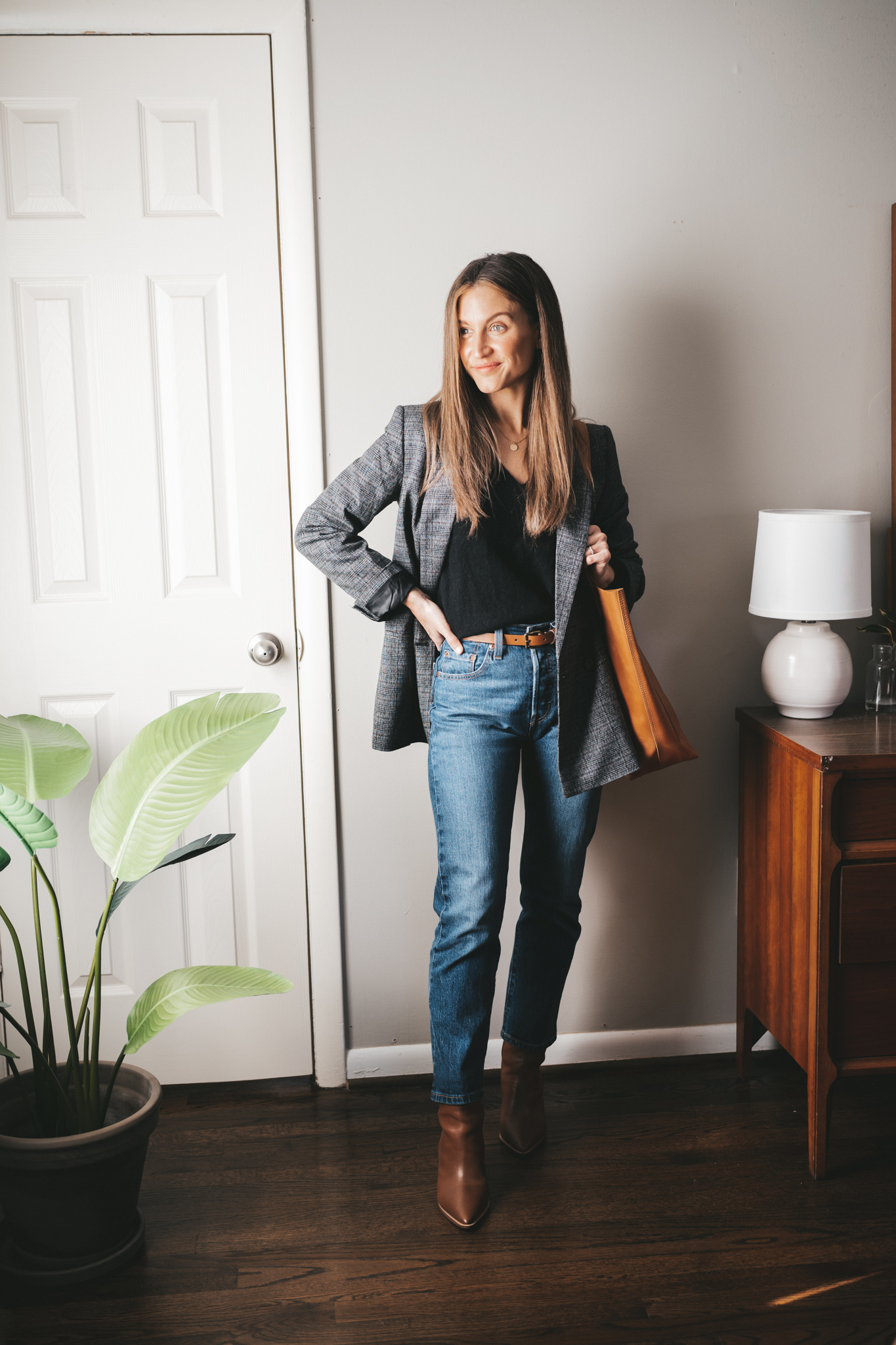 winter capsule wardrobe outfit with a black v-neck sweater, gray plaid blazer, dark wash straight denim, brown ankle boots, and a cognac leather tote bag
