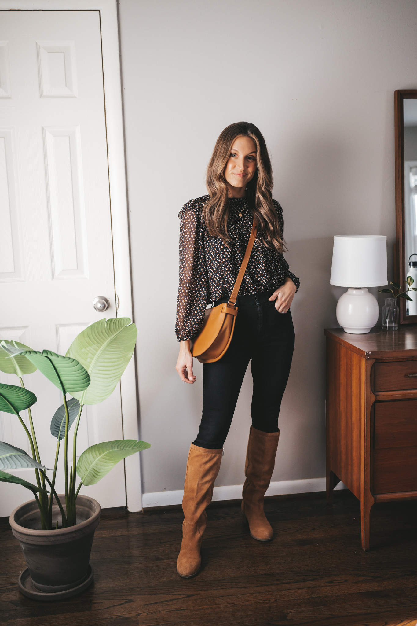 winter capsule wardrobe outfit with a black floral blouse, black skinny jeans, brown suede knee high boots, and a cognac crossbody bag