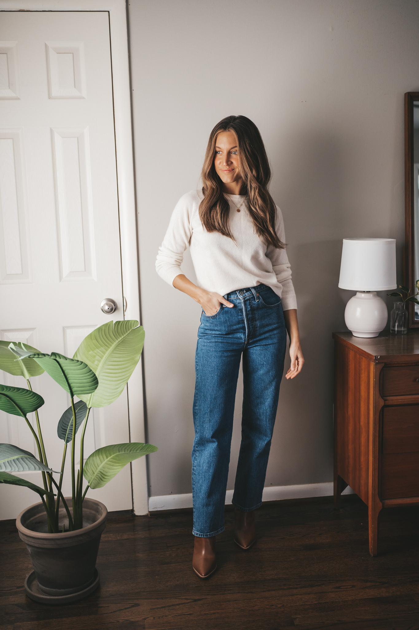 winter capsule wardrobe cashmere crewneck sweater in cream worn with straight leg denim and brown ankle boots
