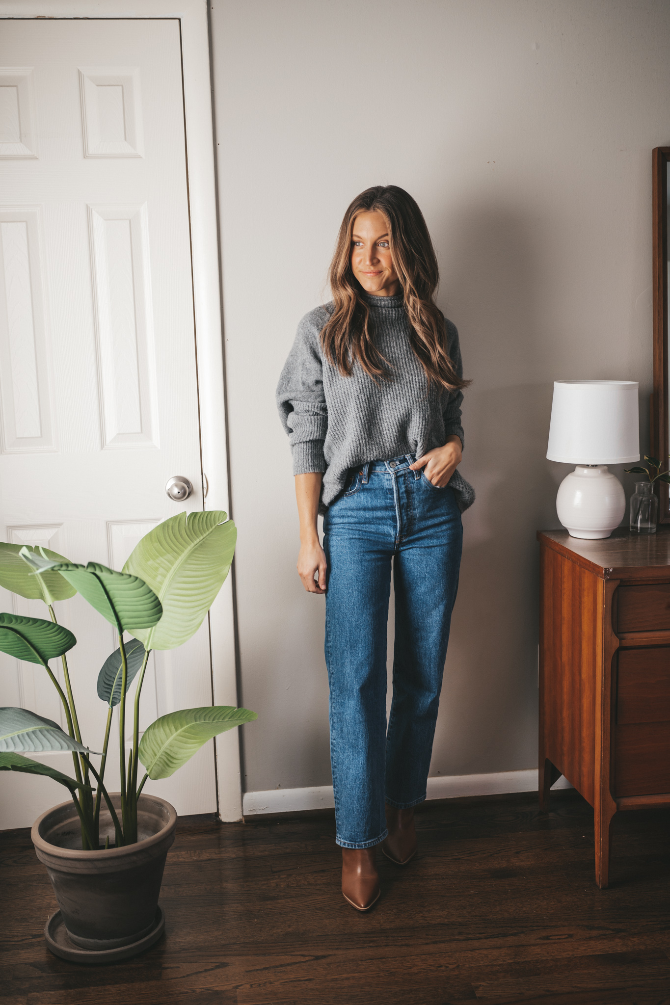 winter capsule wardrobe ABLE mockneck sweater worn with mid-wash denim and brown ankle boots