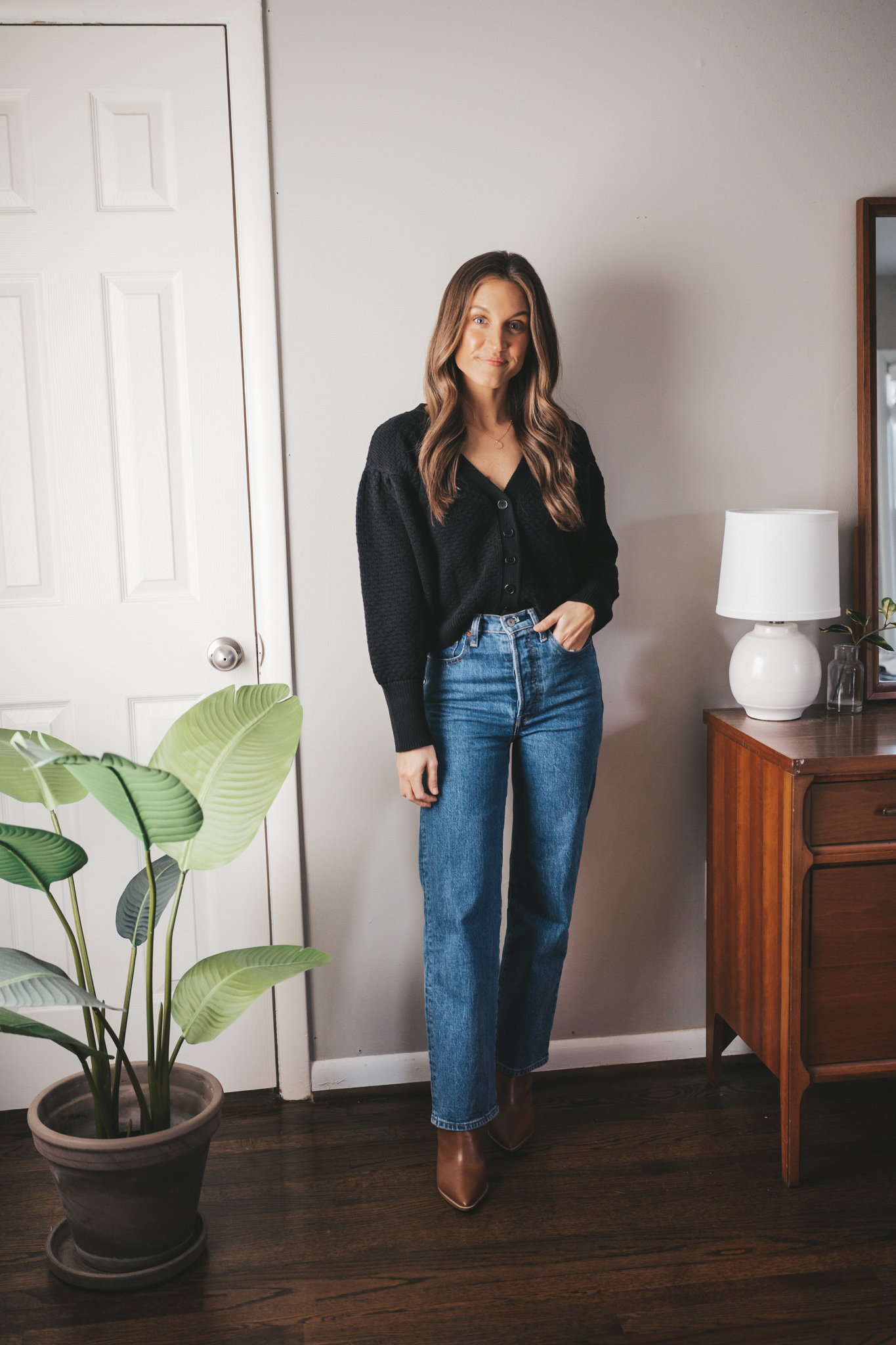 winter capsule wardrobe black button front cardigan worn with mid-wash denim, and brown ankle boots