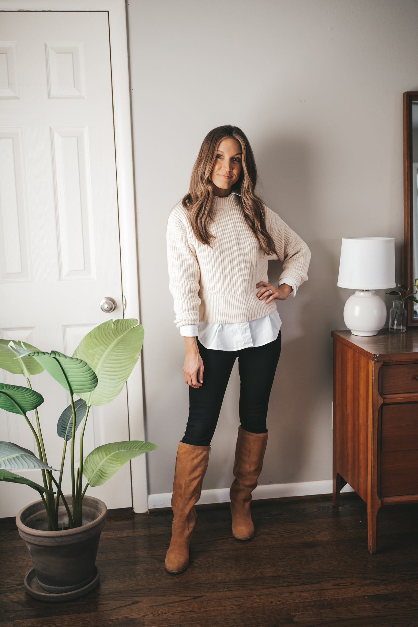 ashley wearing a cream colored crewneck sweater over a white button down, black skinny jeans, and cognac suede ankle boots