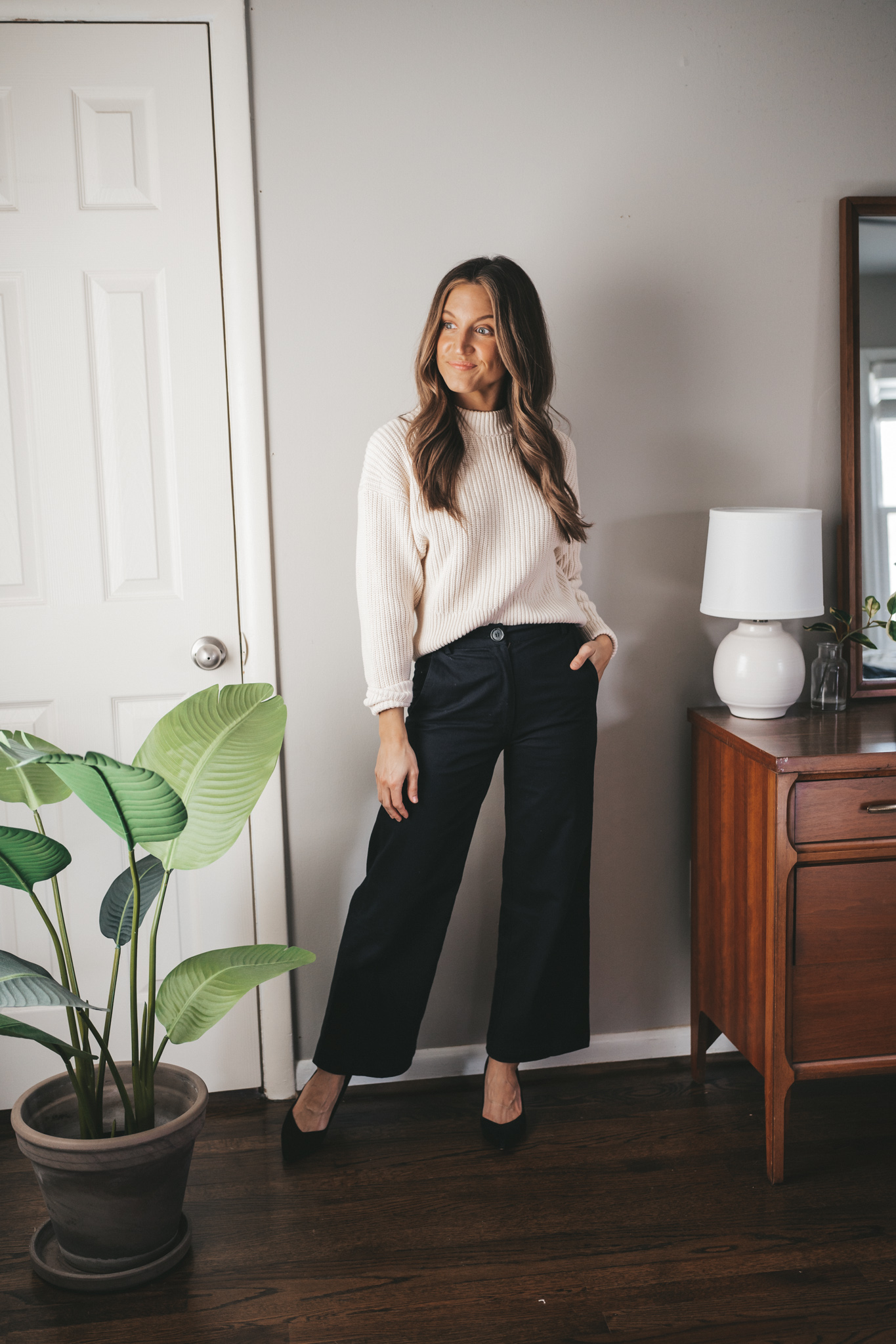 ashley wearing a cream colored crewneck sweater, black wide leg pants, and black block heel pumps