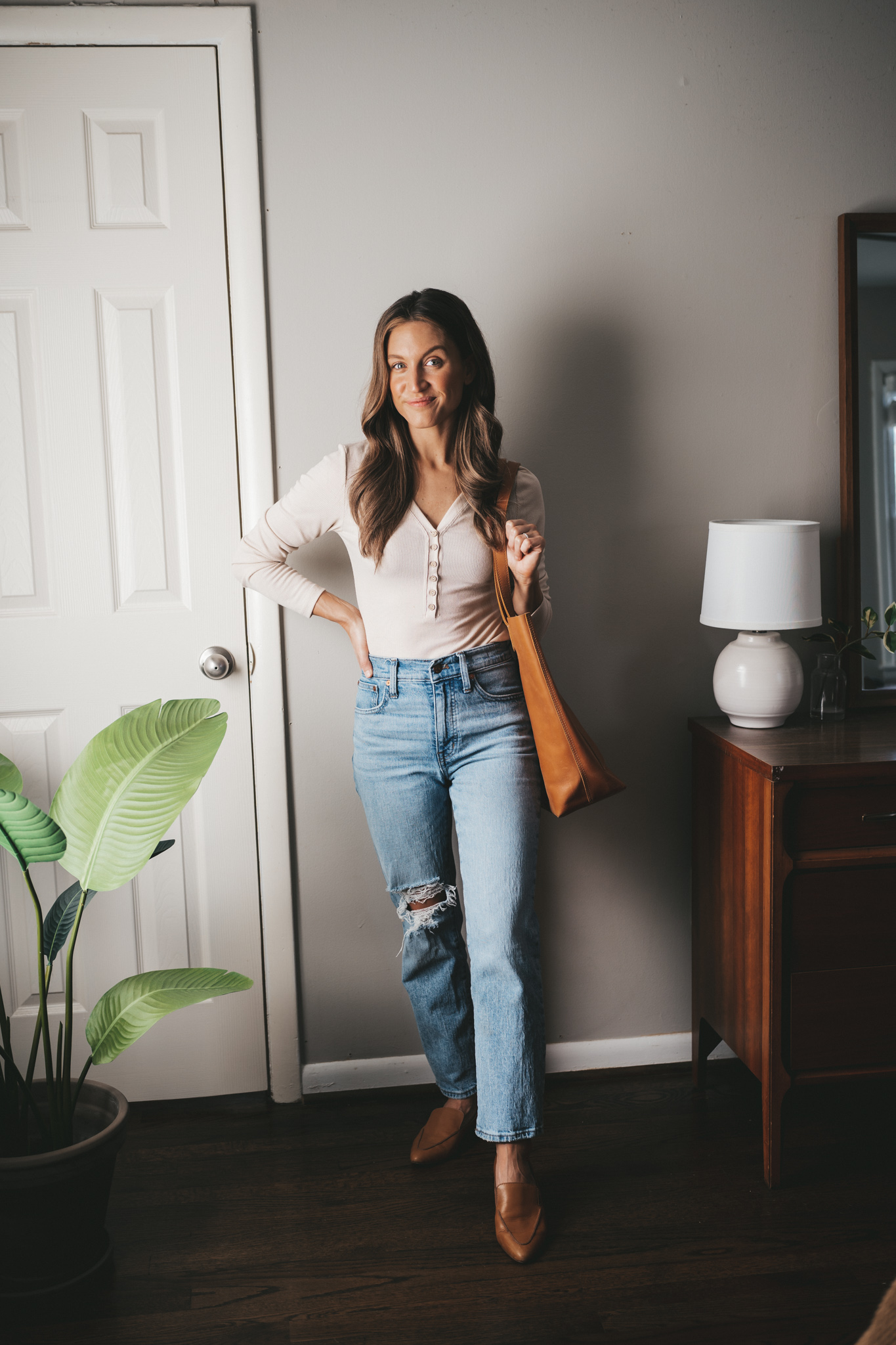 winter capsule wardrobe outfit idea with a ivory henley bodysuit, light wash distressed denim, cognac loafers, and a cognac leather tote bag