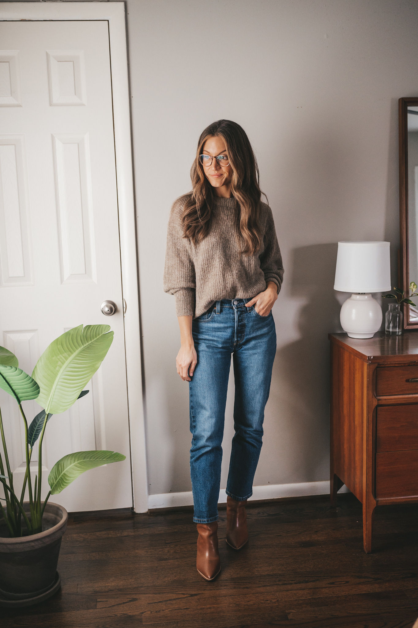 winter capsule wardrobe outfit idea with a taupe crewneck oversized sweater, dark wash denim, and brown ankle boots
