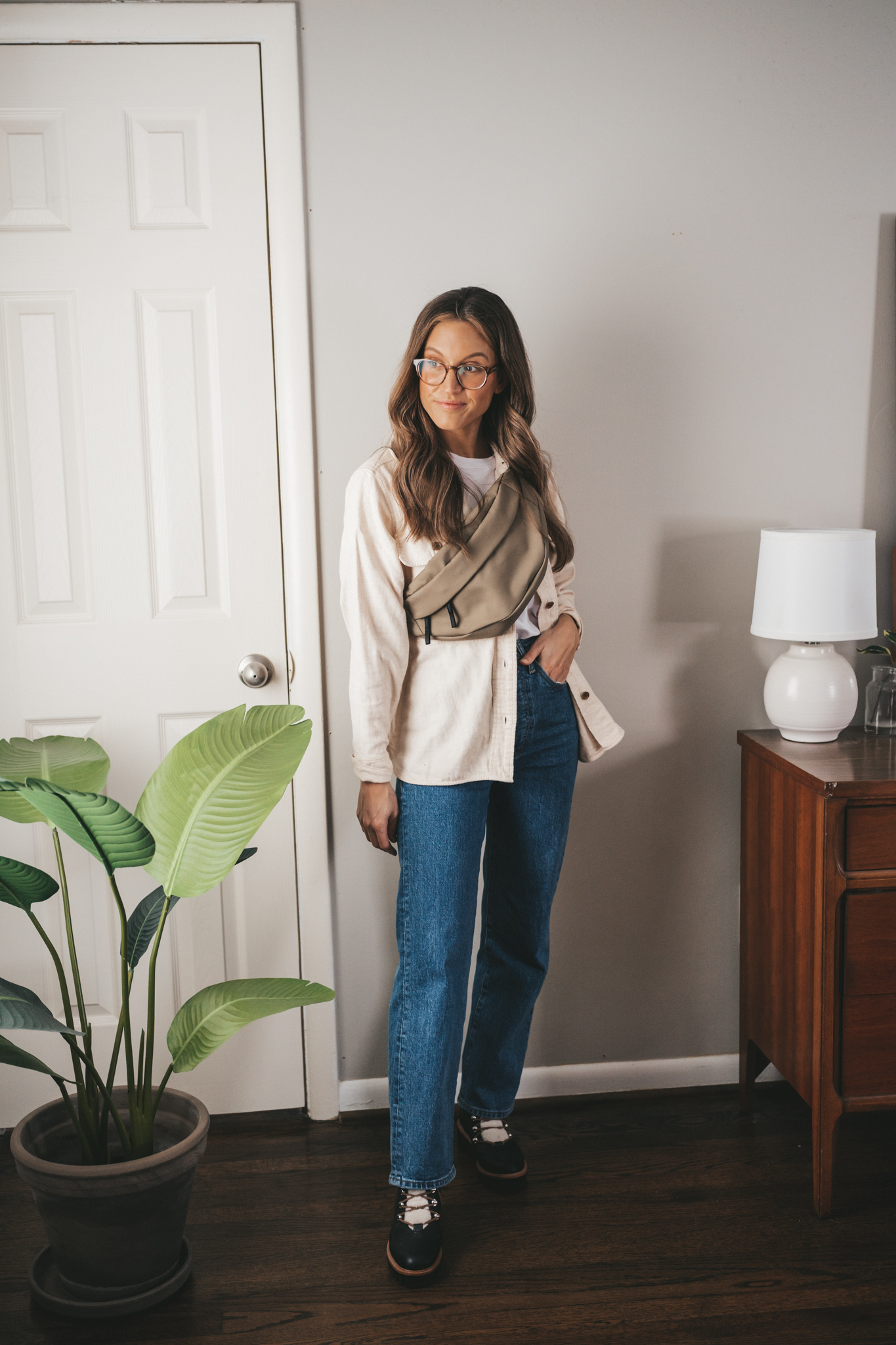 winter capsule wardrobe outfit idea with a white tee under a cream colored flannel, straight dark wash denim, faux shearling lace up black winter boots, and an olive green belt bag