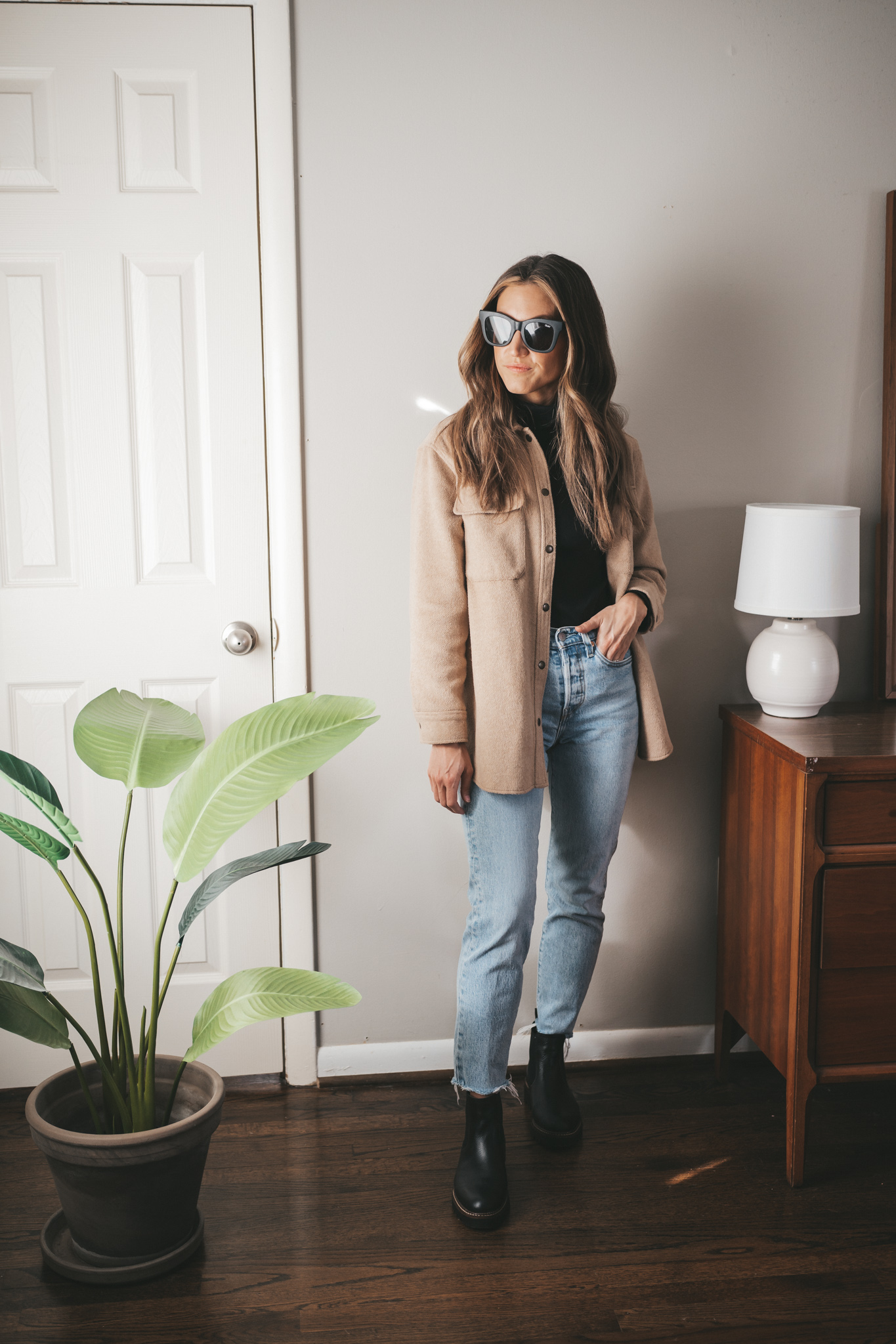 winter outfit idea with a black turtleneck, tan shacket, light wash mom jeans, black lug sole chelsea boots and black square frame sunglasses