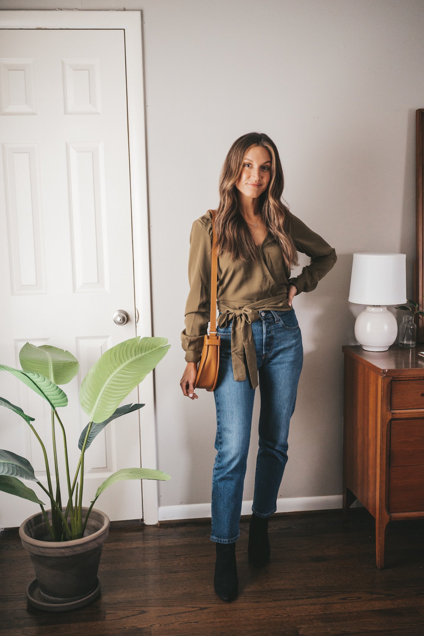 winter outfit idea with an olive green wrap blouse, mid-wash straight denim, black ankle boots, and a cognac crossbody bag
