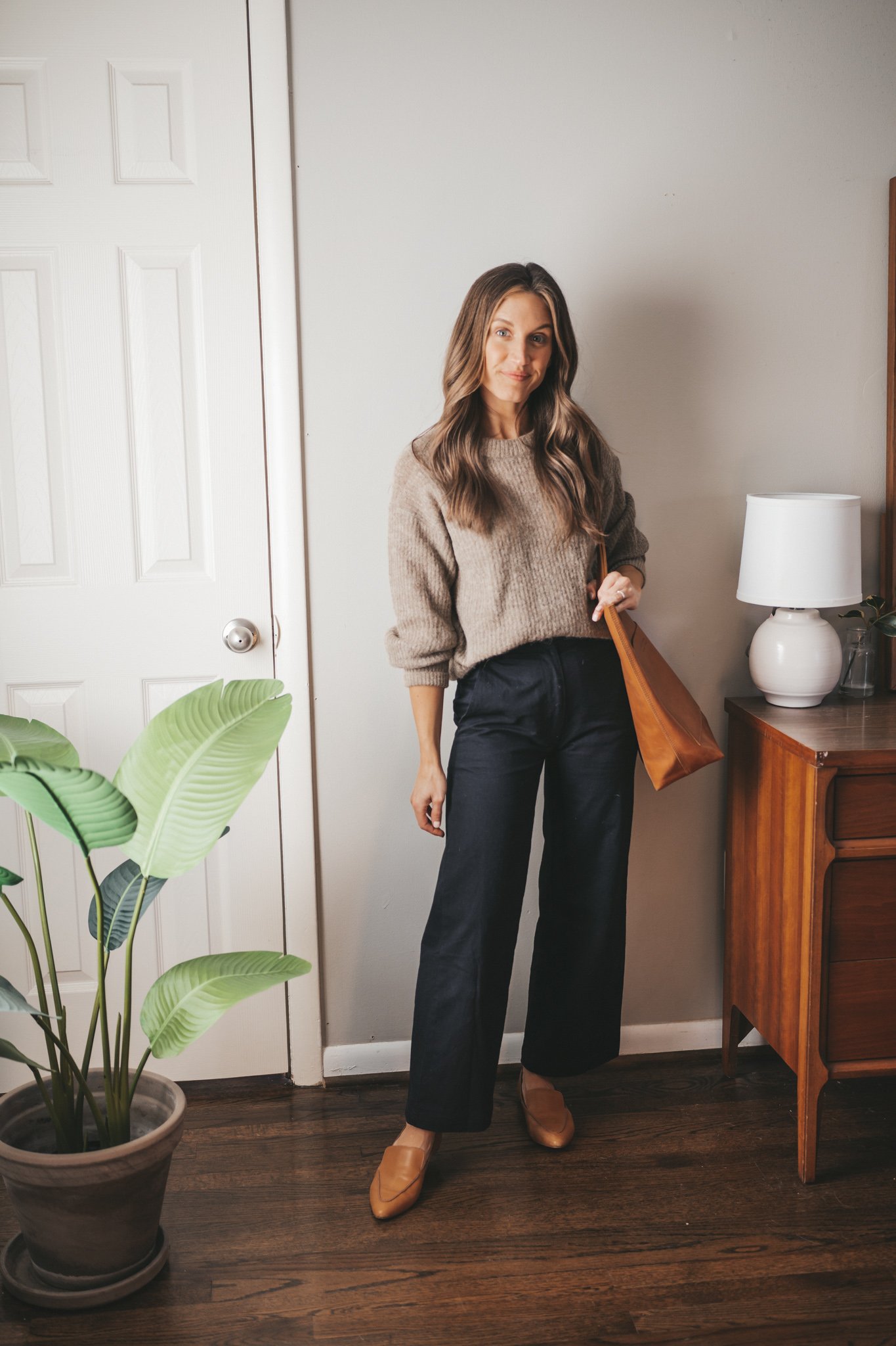 winter outfit idea with a taupe oversized sweater, black wide leg pants, cognac loafers, and a cognac tote bag