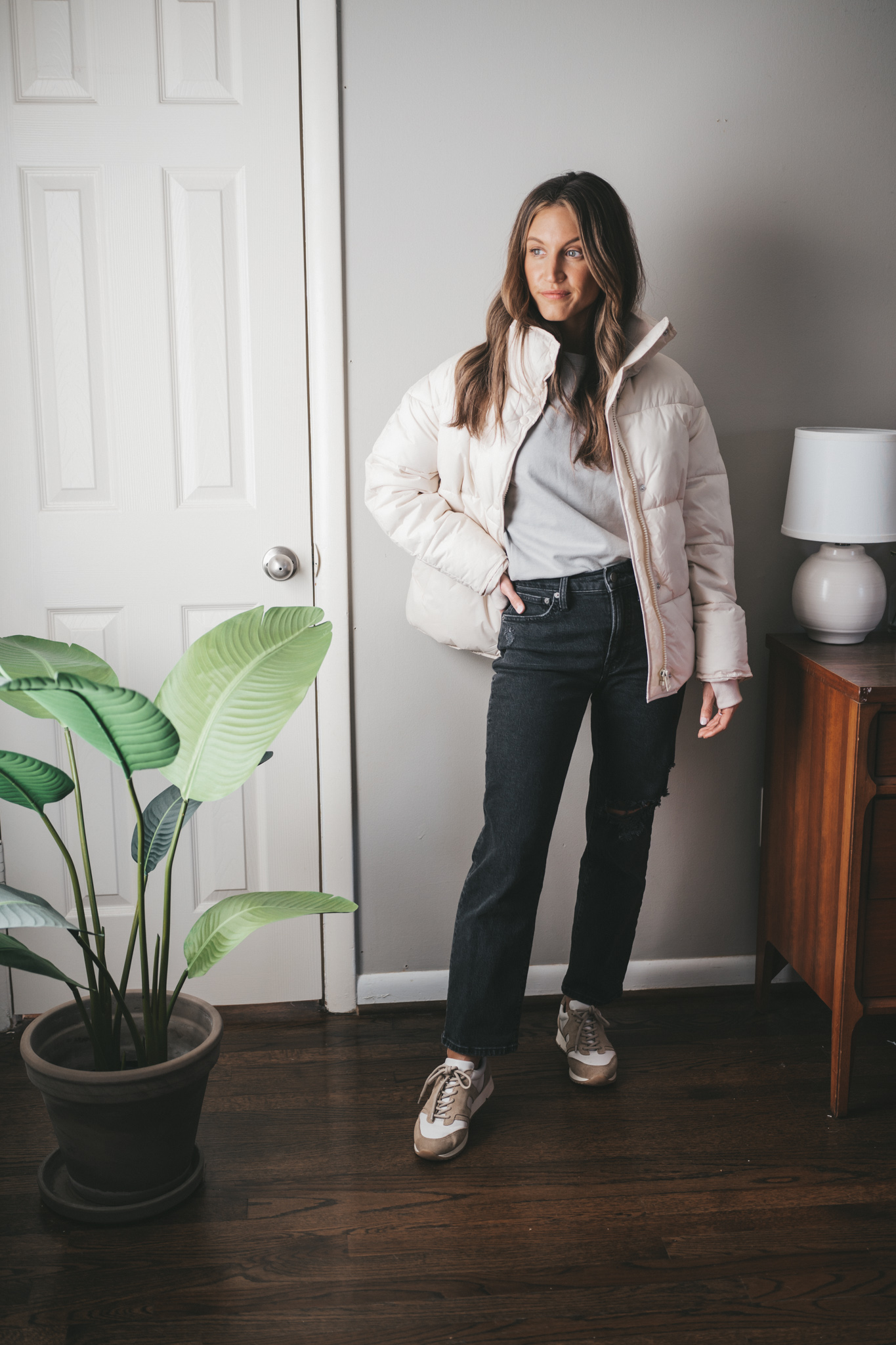 winter outfit idea with a gray sweatshirt, white puffer coat, washed black denim, and white and tan sneakers