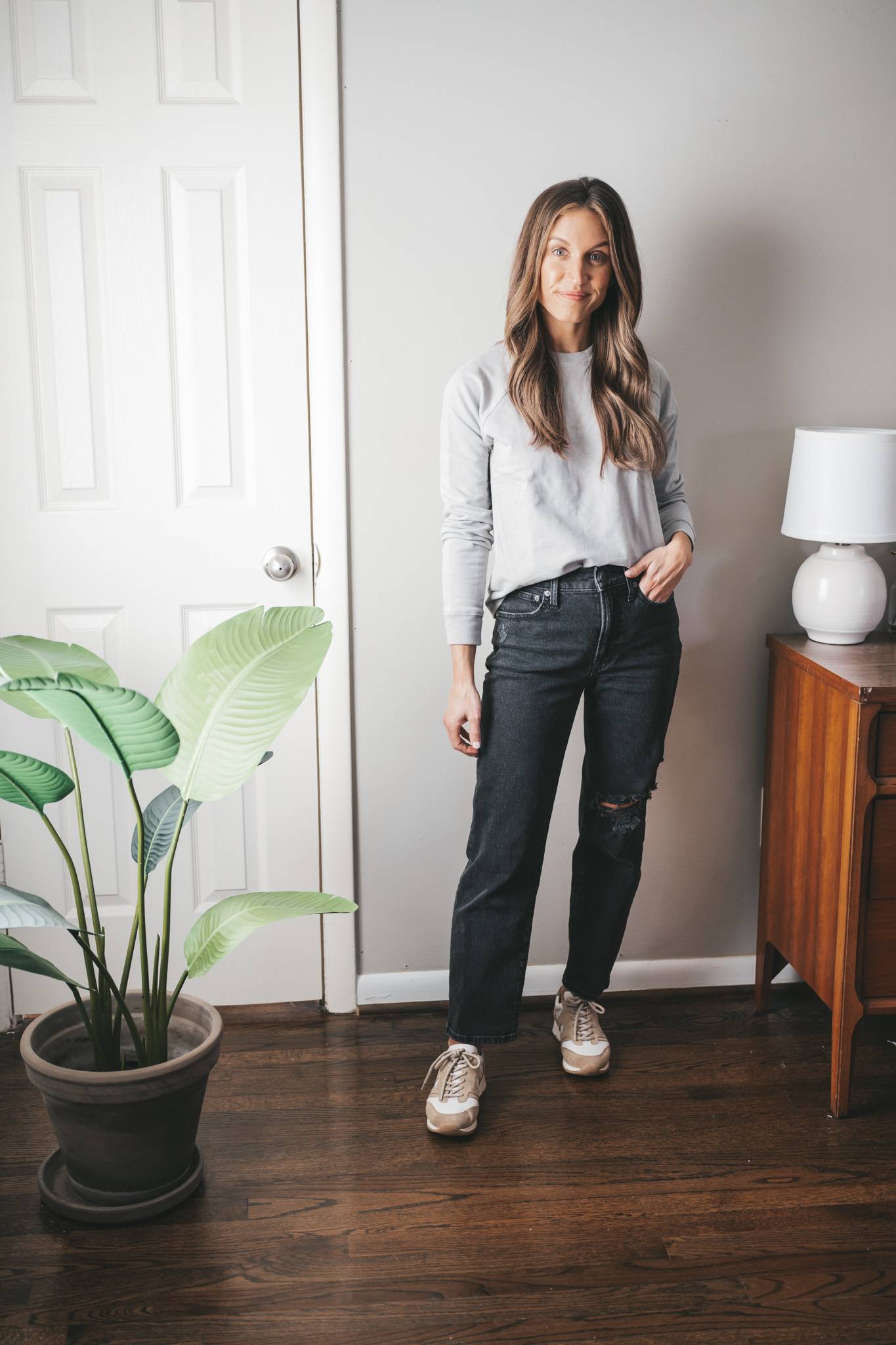 winter outfit with a gray sweatshirt, washed black straight denim, and white and tan leather sneakers