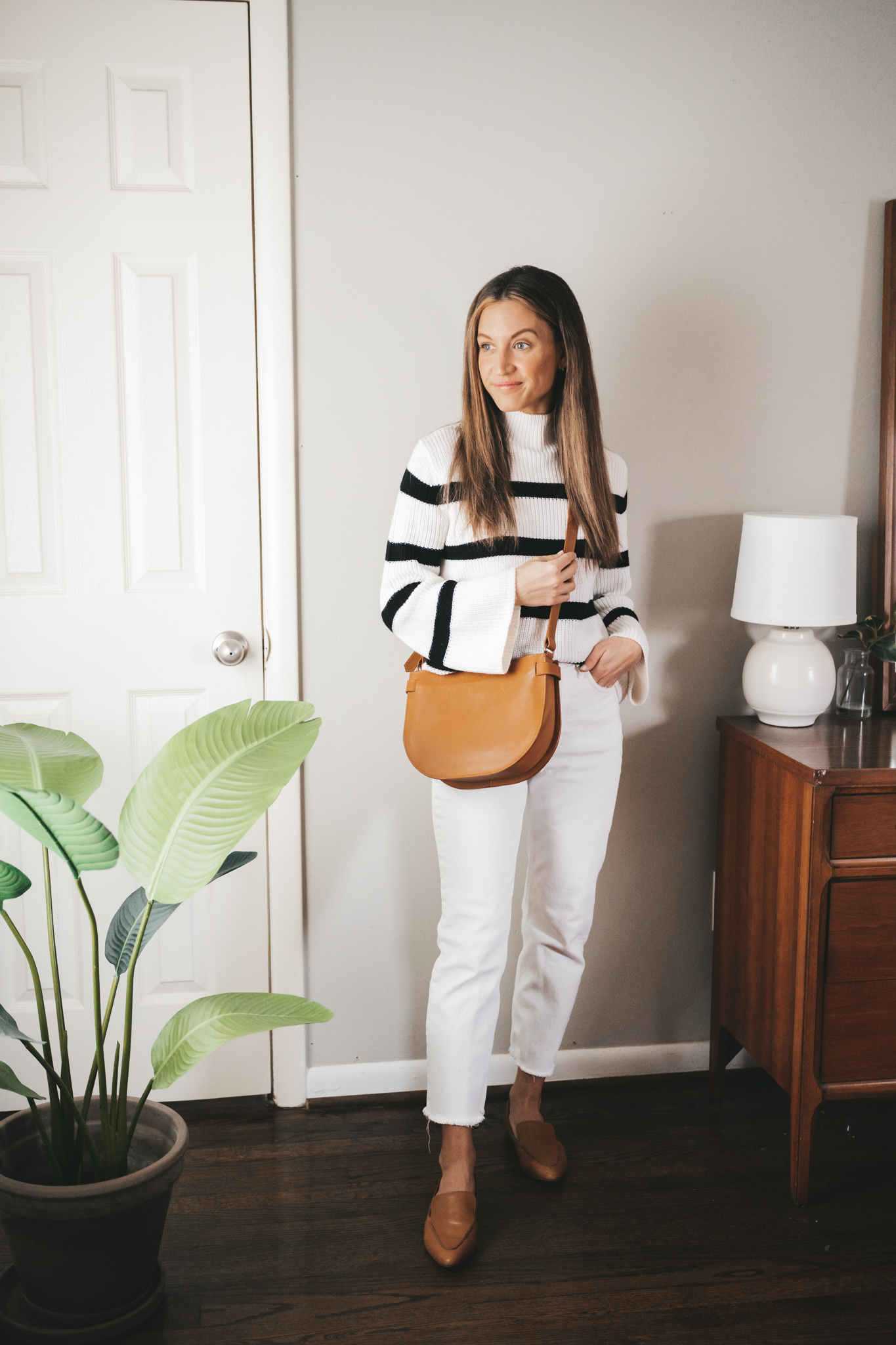 winter capsule wardrobe outfit with a white and black striped sweater, white denim, cognac loafers, and a cognac tote bag