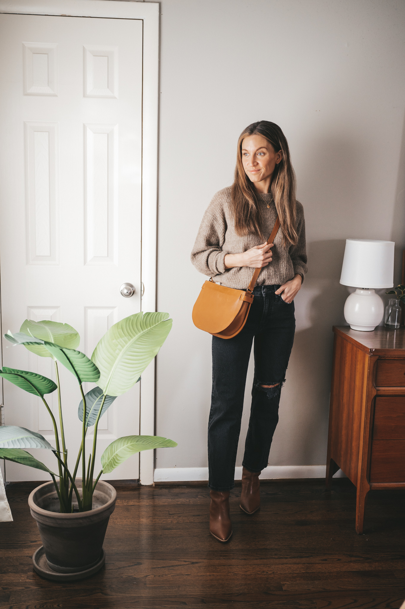 winter capsule wardrobe outfit with a taupe oversized sweater, black distressed denim, brown ankle boots and a cognac crossbody bag